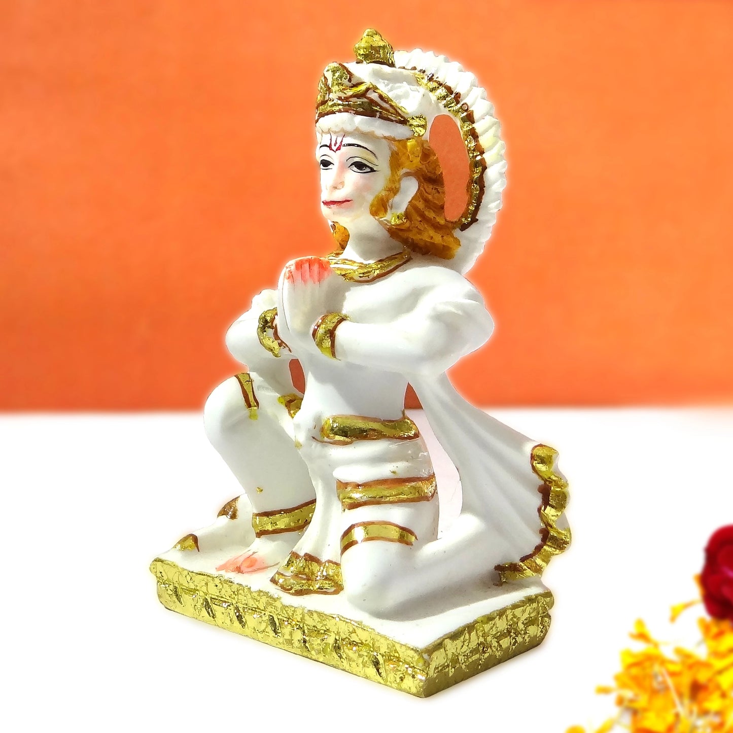 White and gold figurine of a seated deity on an orange background