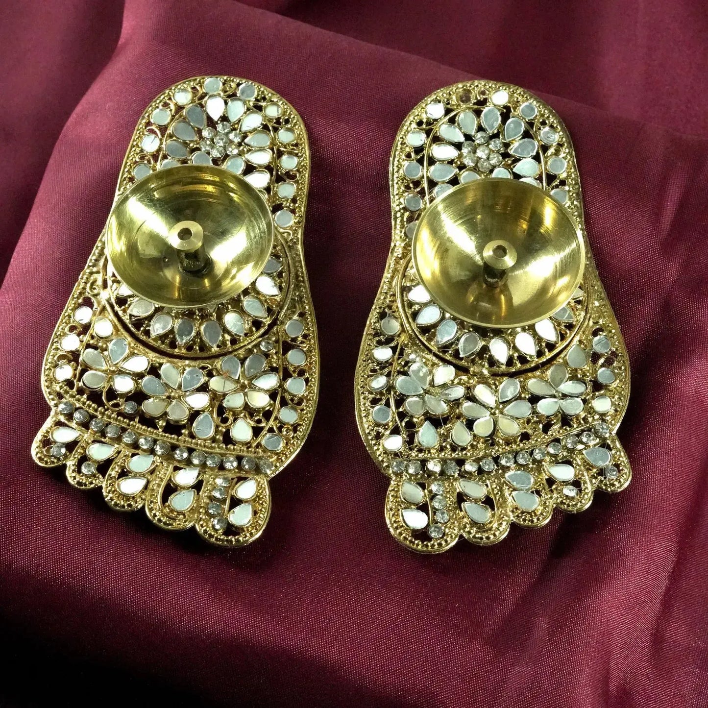 Pair of gold earrings with intricate designs on a maroon fabric background