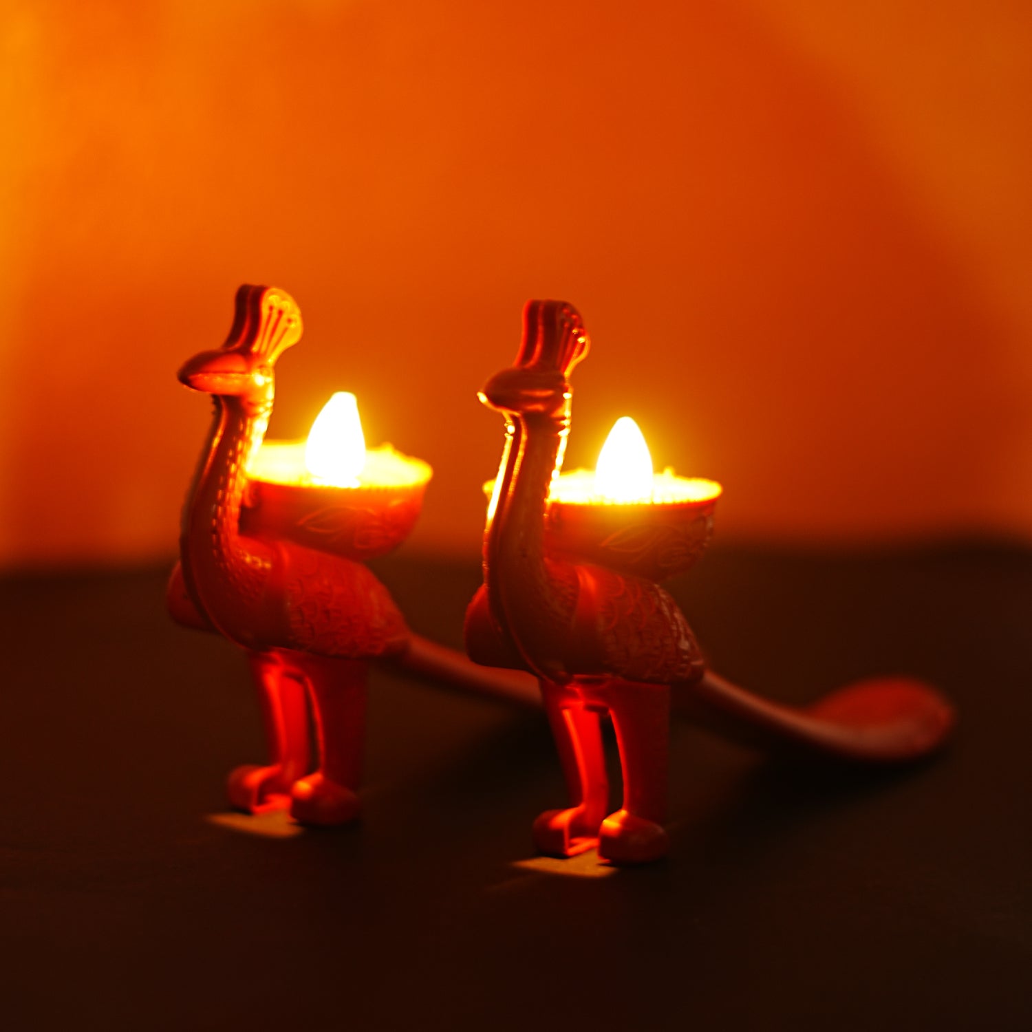 Two peacock-shaped candles with lit candles inside on a dark background
