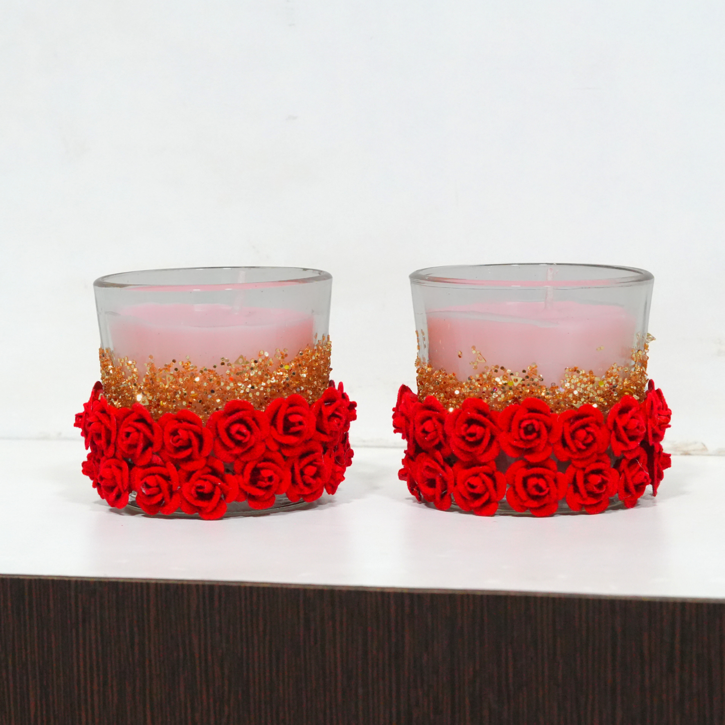 Two candle holders with red rose decorations on a white surface.