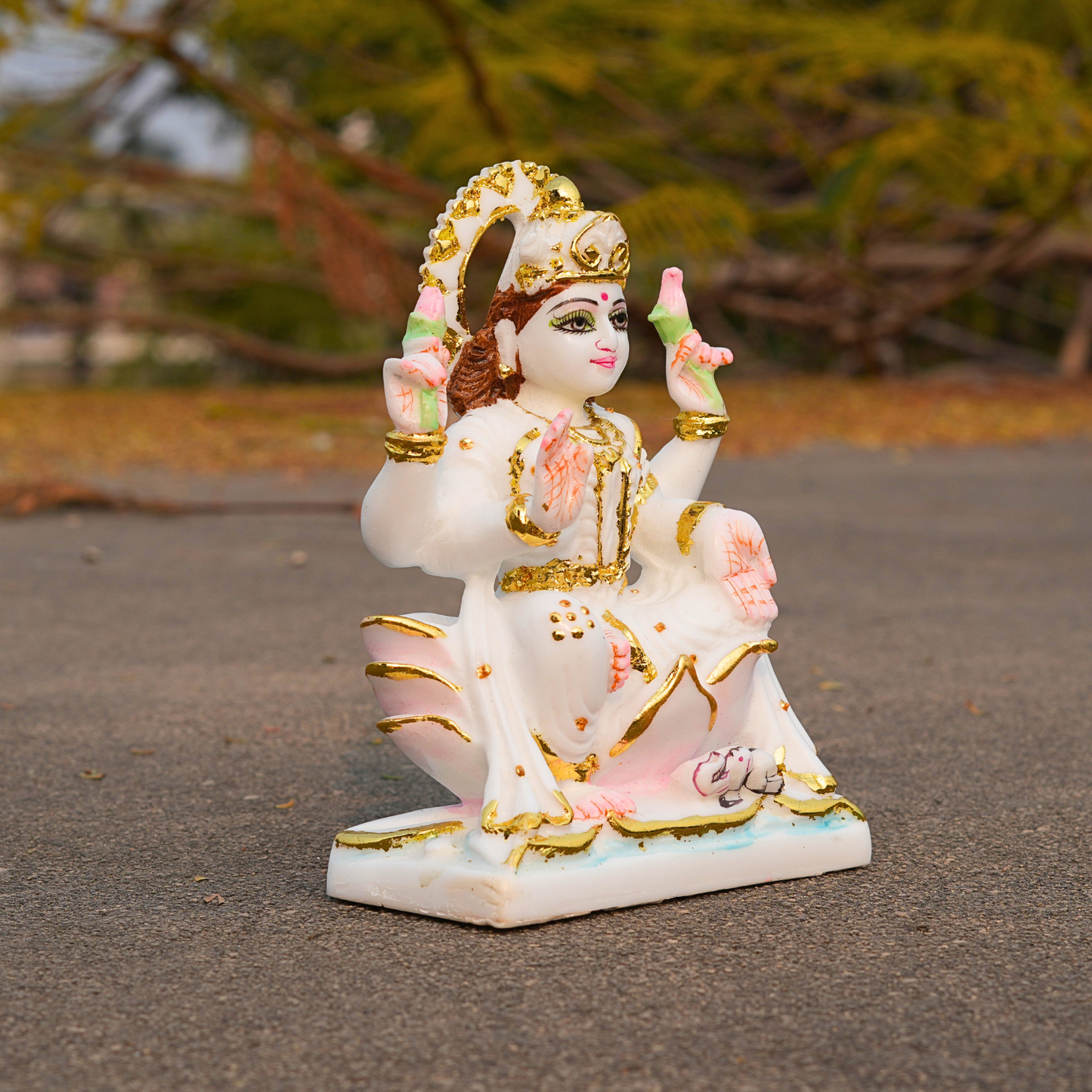 Decorative statue of a seated figure with gold and pink accents on a blurred natural background