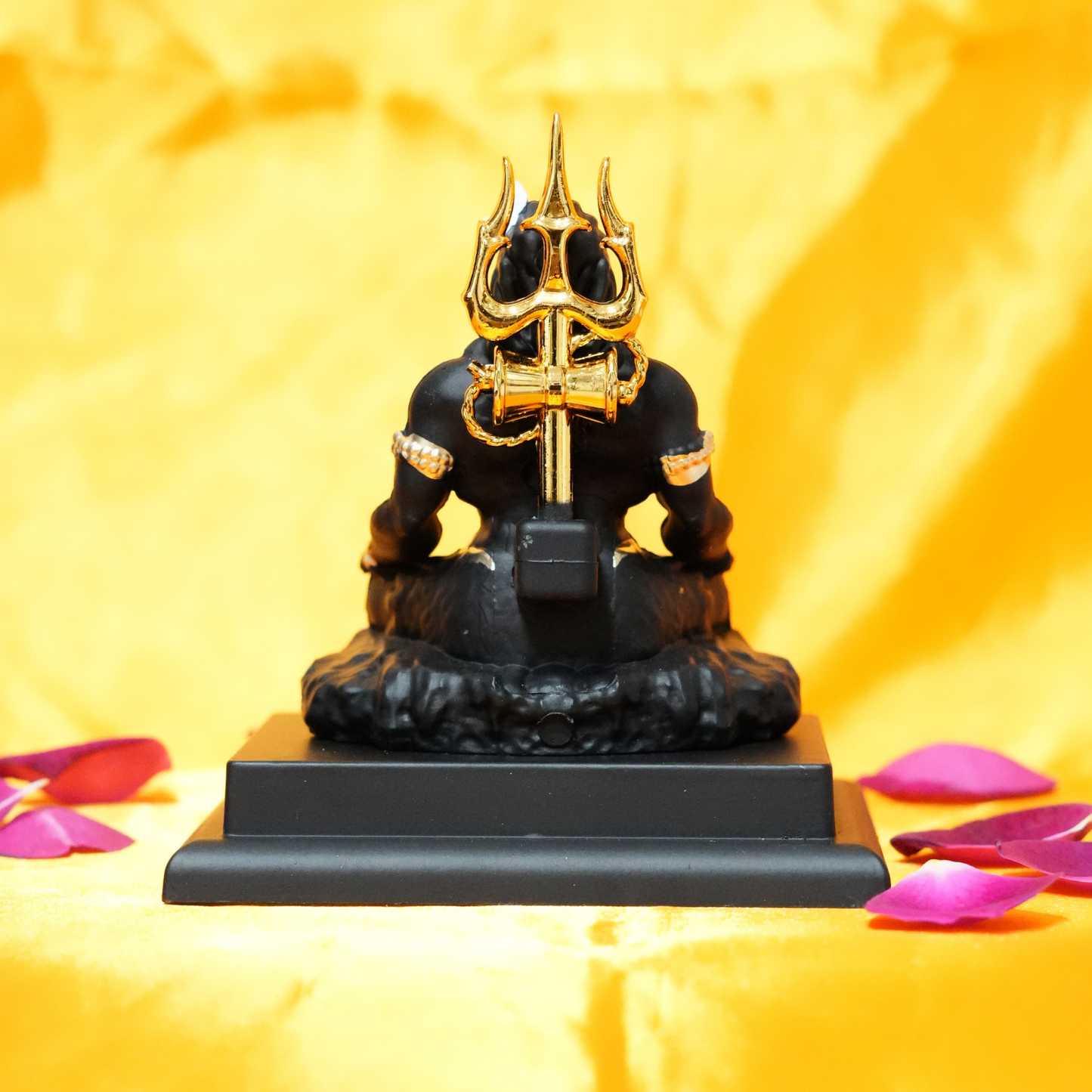 Black and gold figurine on a yellow background with pink petals