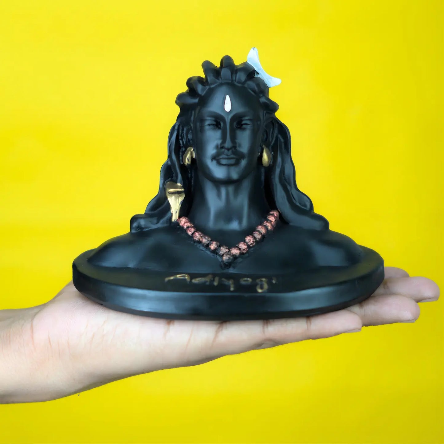 Black statue of a deity held in a hand against a yellow background