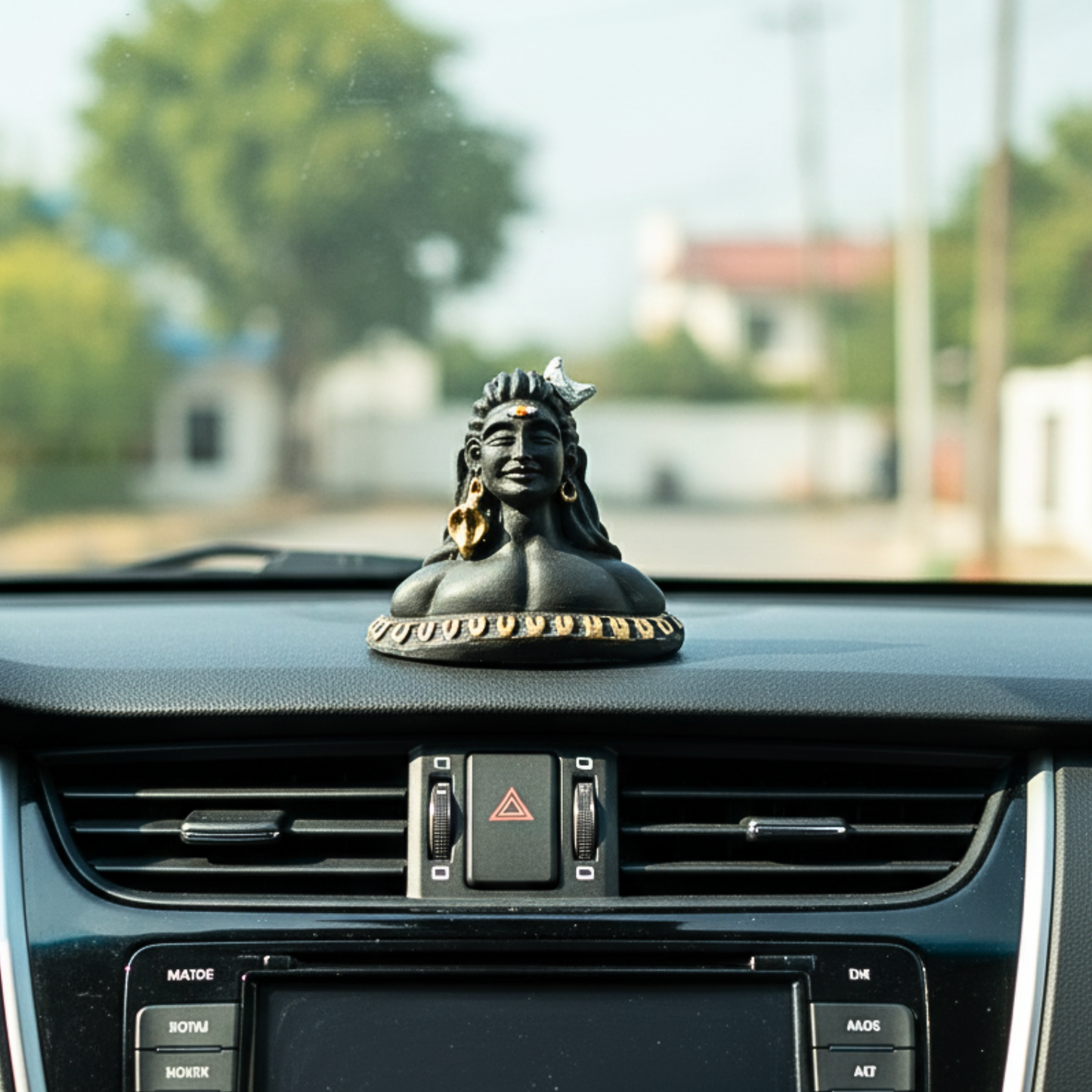 Car dashboard with a decorative figure on top, blurred outdoor background