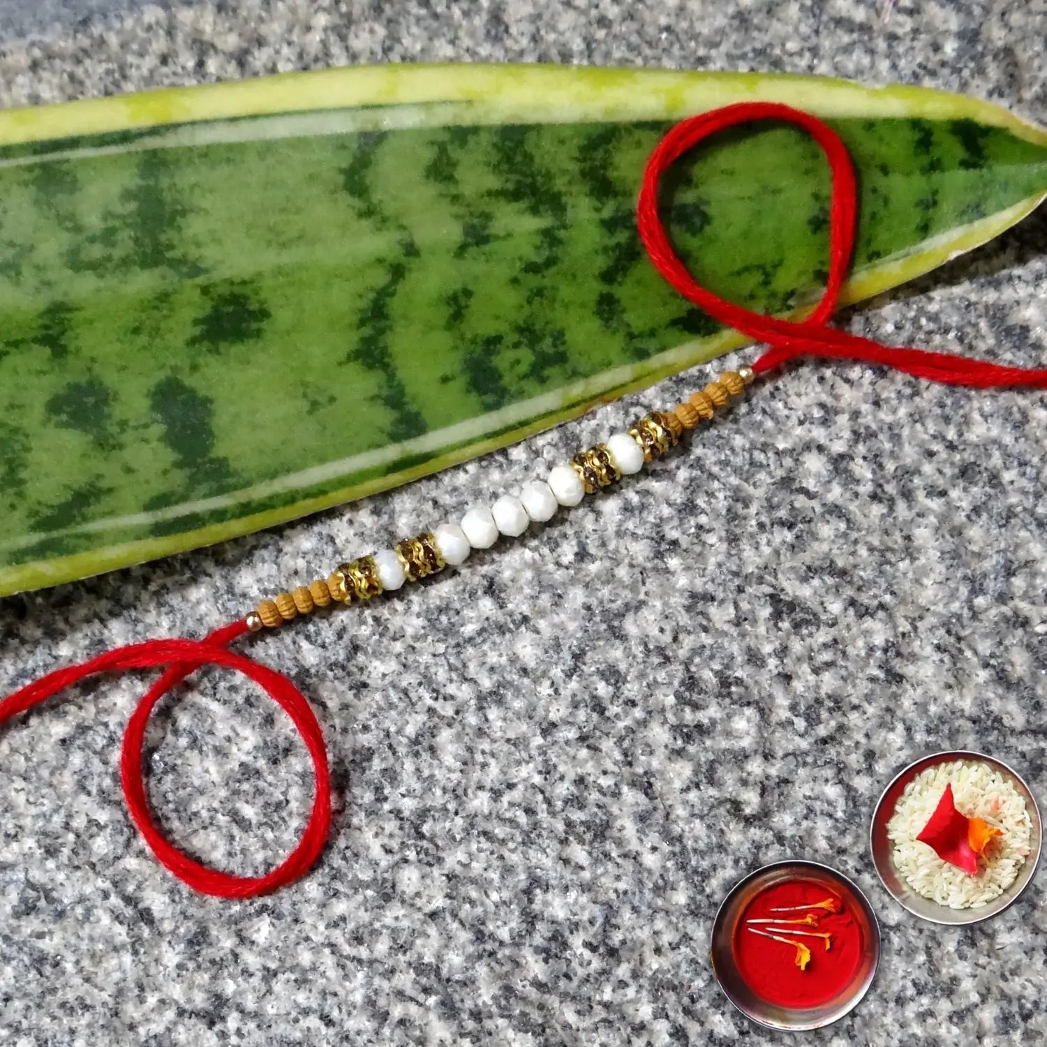 Beaded bracelet with red thread on a leaf, placed on a textured surface with small decorative items.