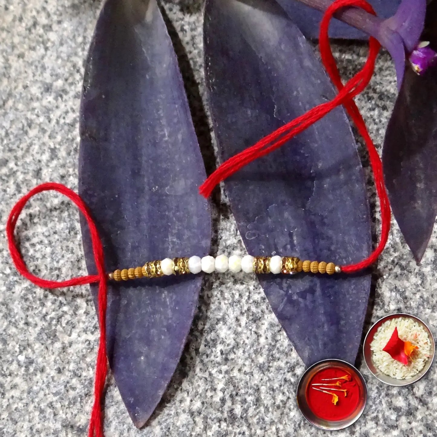 Bracelet with red thread on purple sandal, with small bowls of rice and flowers in the background.