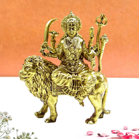 Gold-colored statue of a deity sitting on a lion with a pink background