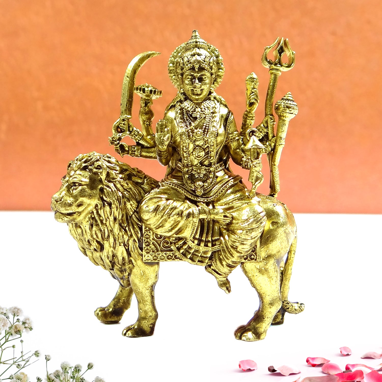 Gold-colored statue of a deity sitting on a lion with a pink background