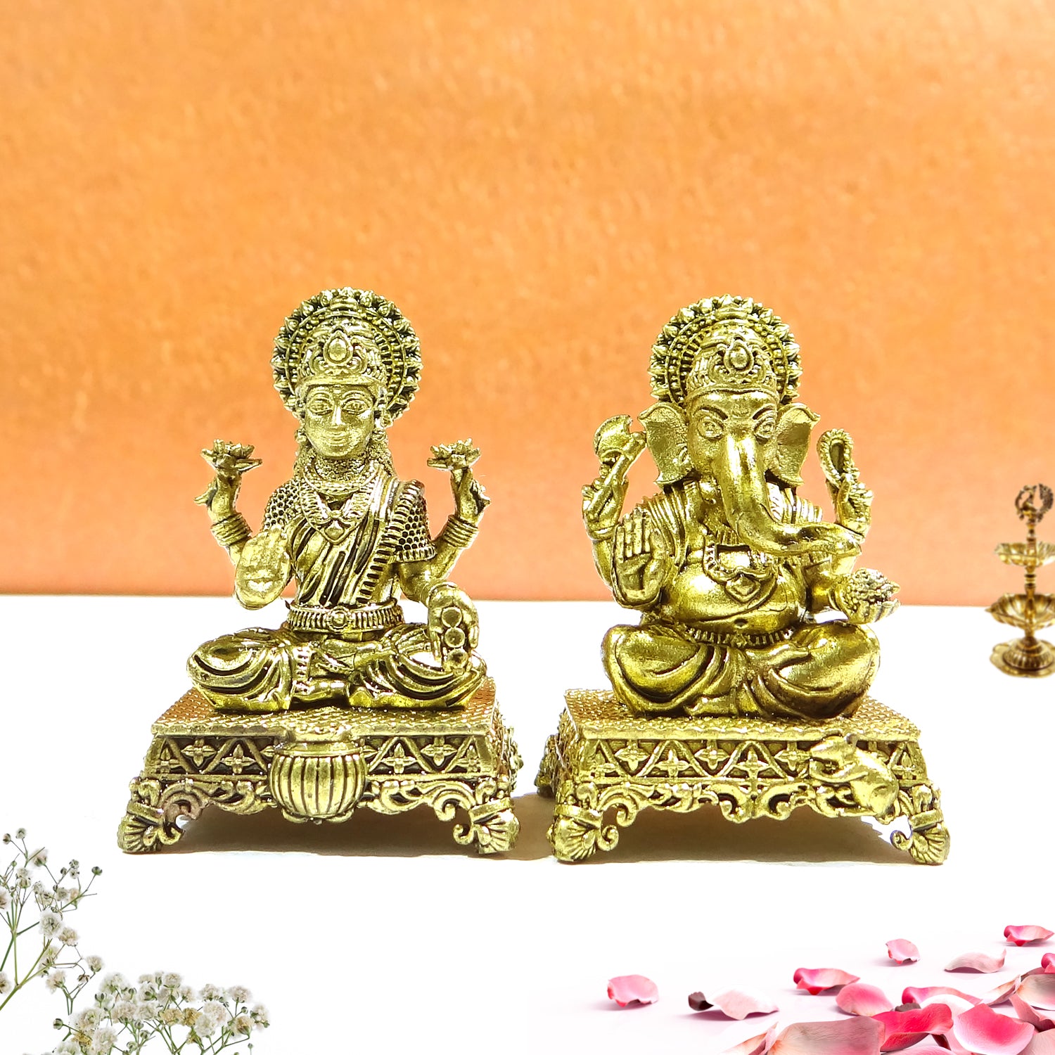 Two gold-colored statues of deities on decorative stands against an orange background.