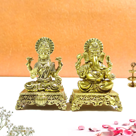 Two gold-colored statues of deities on decorative stands against an orange background.