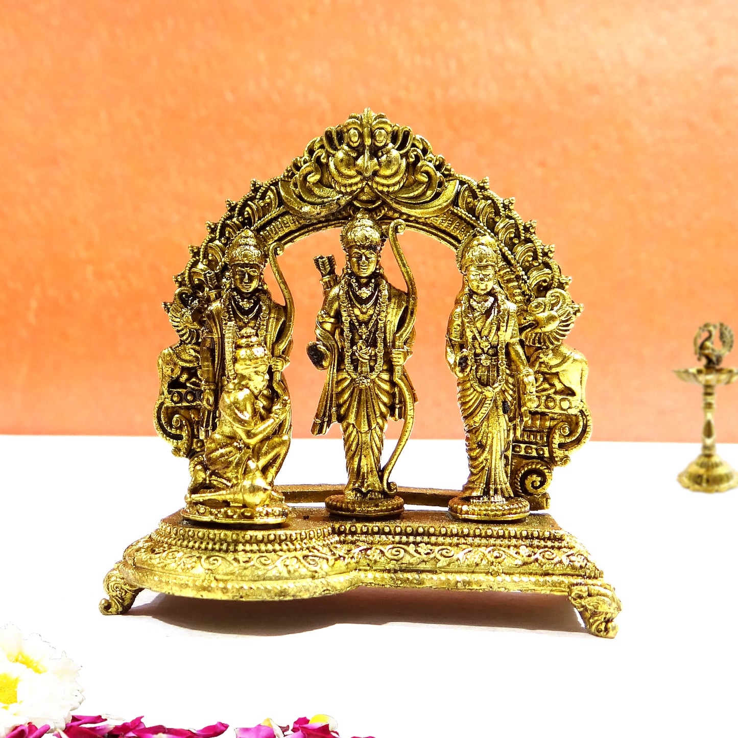 Decorative gold statue of three figures on a white surface with an orange background