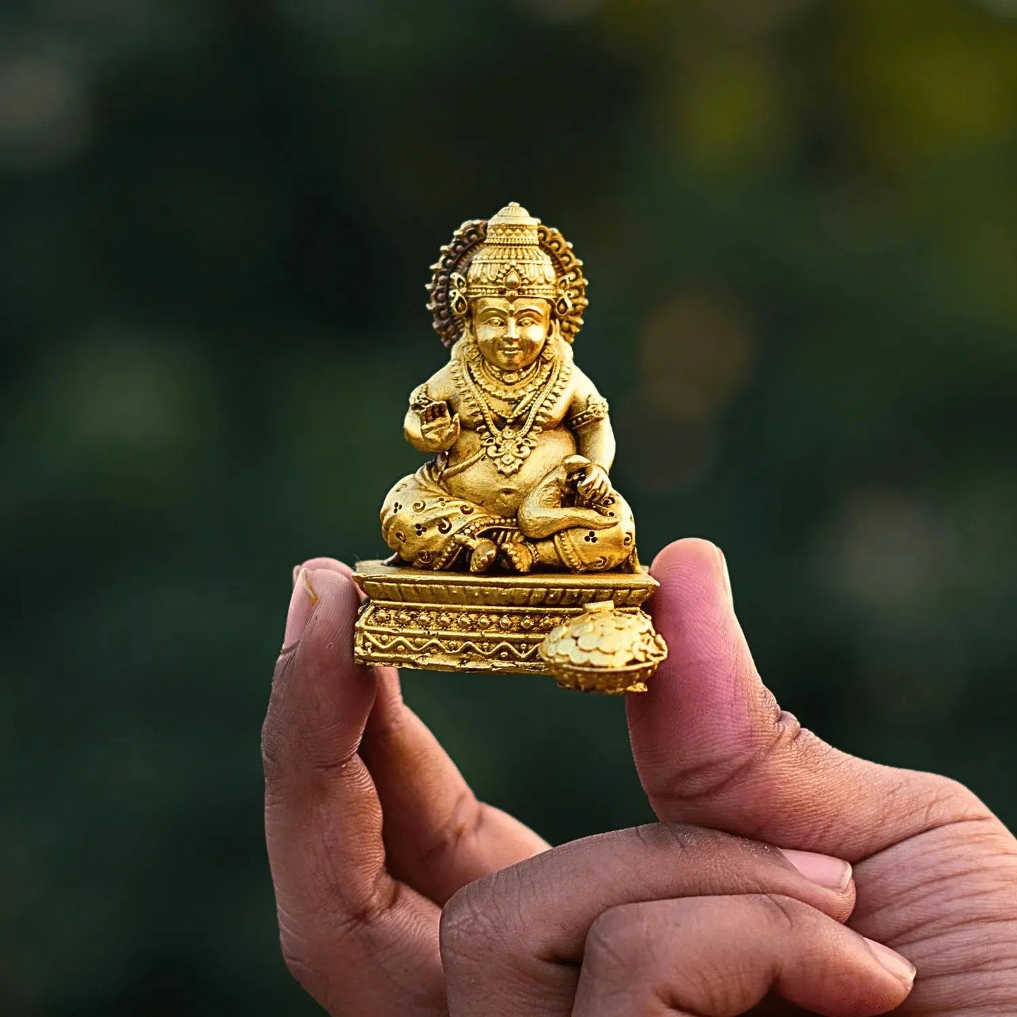 Gold-colored statue held in a hand with a blurred green background