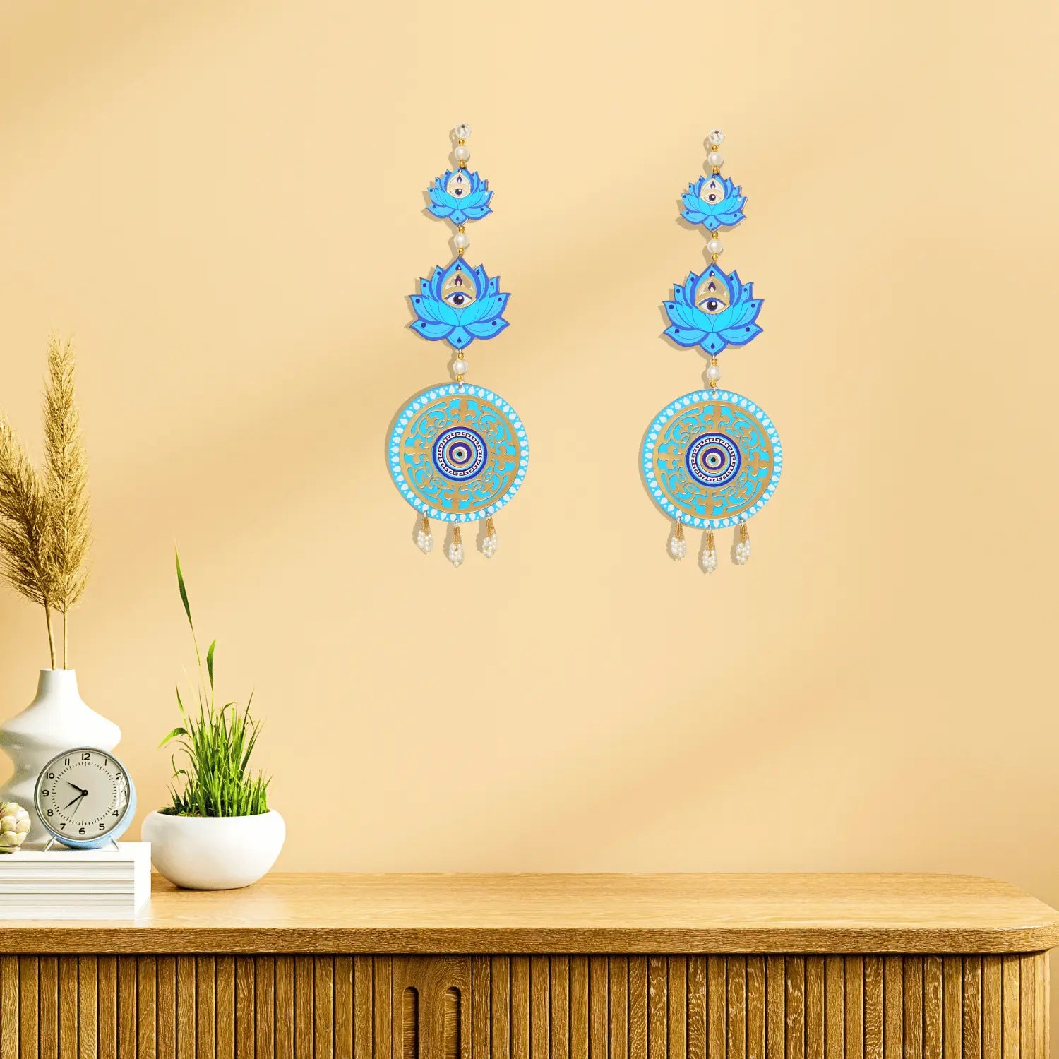 Decorative earrings with blue and gold designs on a beige wall.
