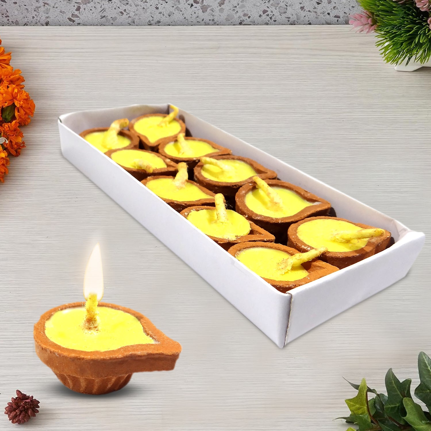 Box of small Diwali candles with one lit candle on a decorative surface.