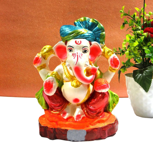 Colorful Ganesha statue with a plant on a white surface against an orange wall