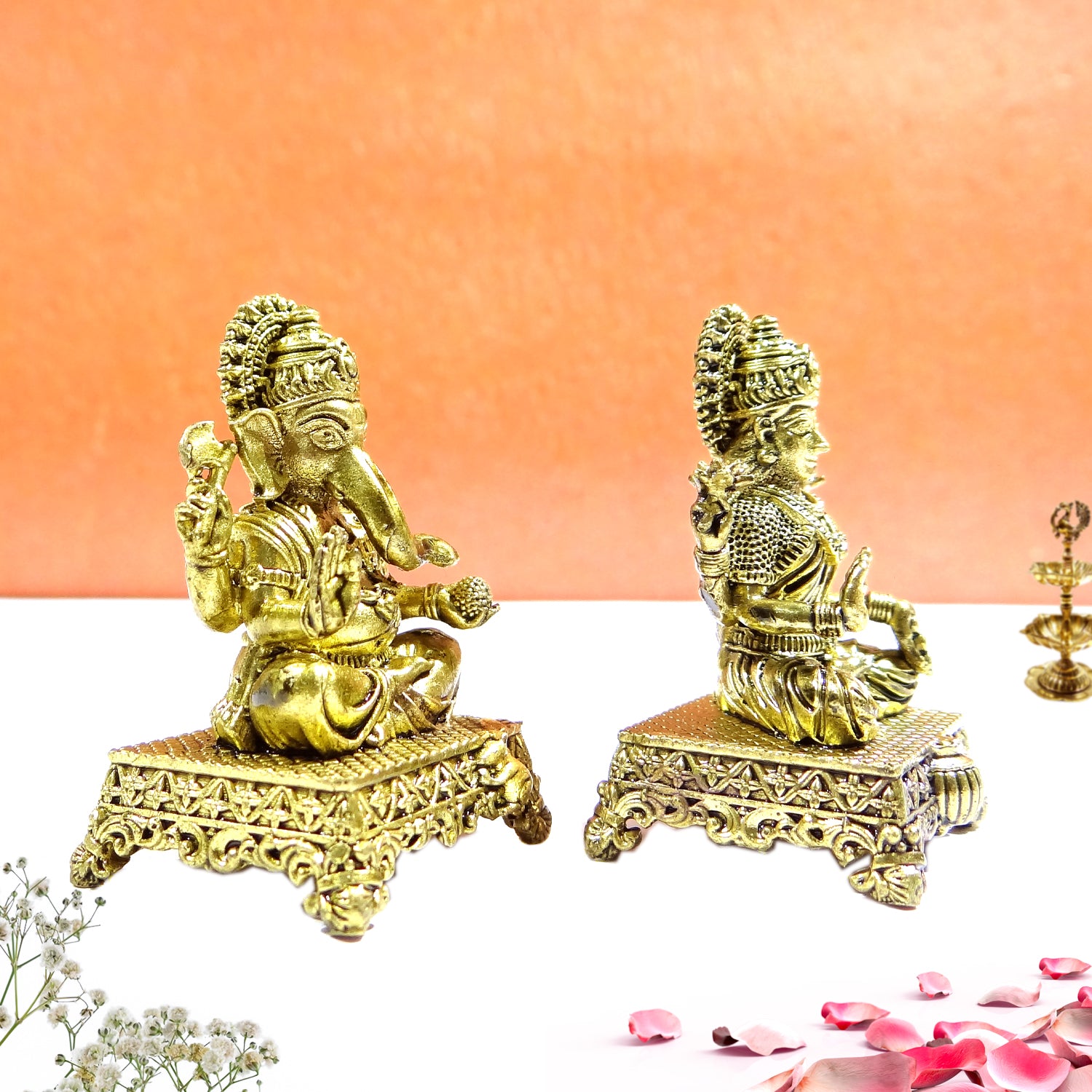Two gold-colored deity statues on decorative stands against a peach background.