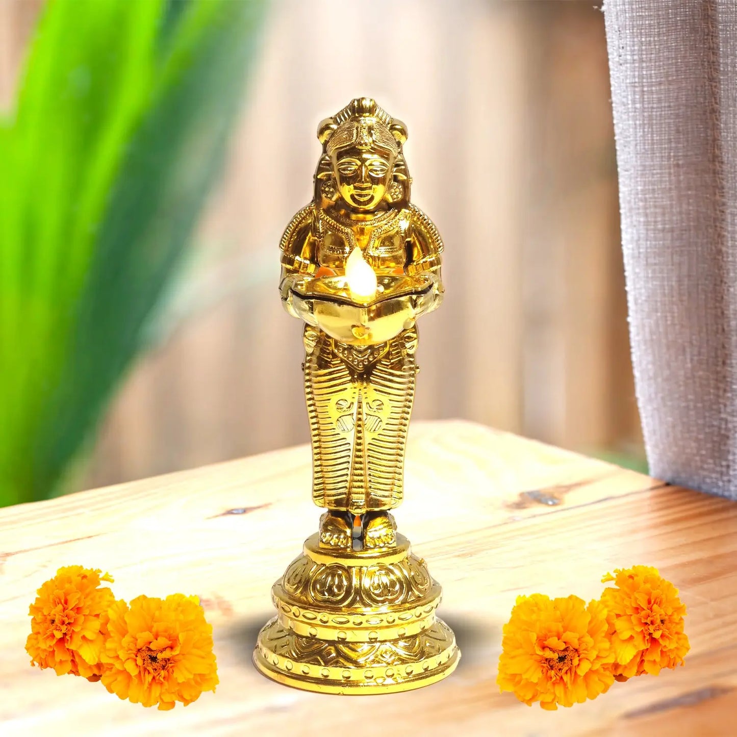 Gold-colored statue with a candle on a wooden surface with marigold flowers.