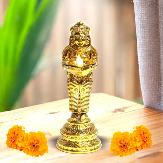 Gold-colored statue with a candle on a wooden surface with marigold flowers.