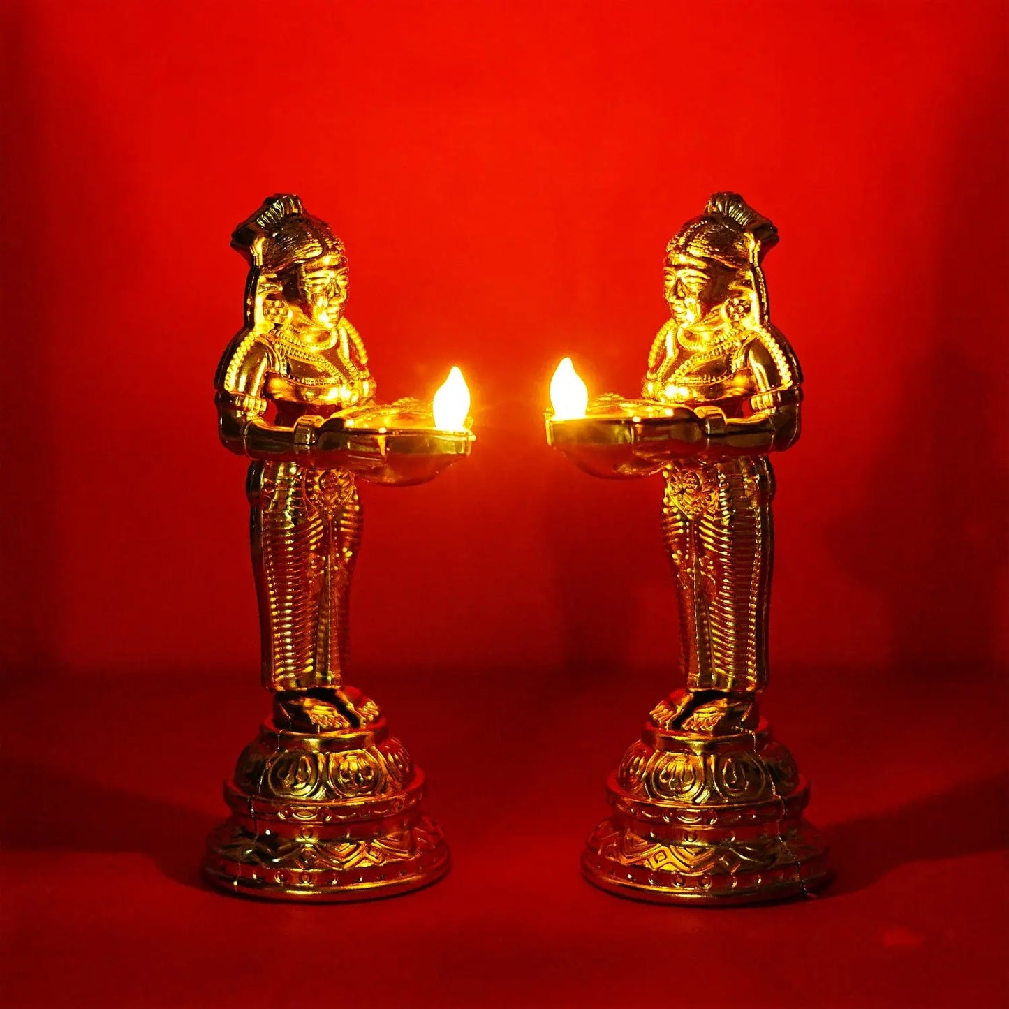 Two gold-colored statues with lit candles on a red background
