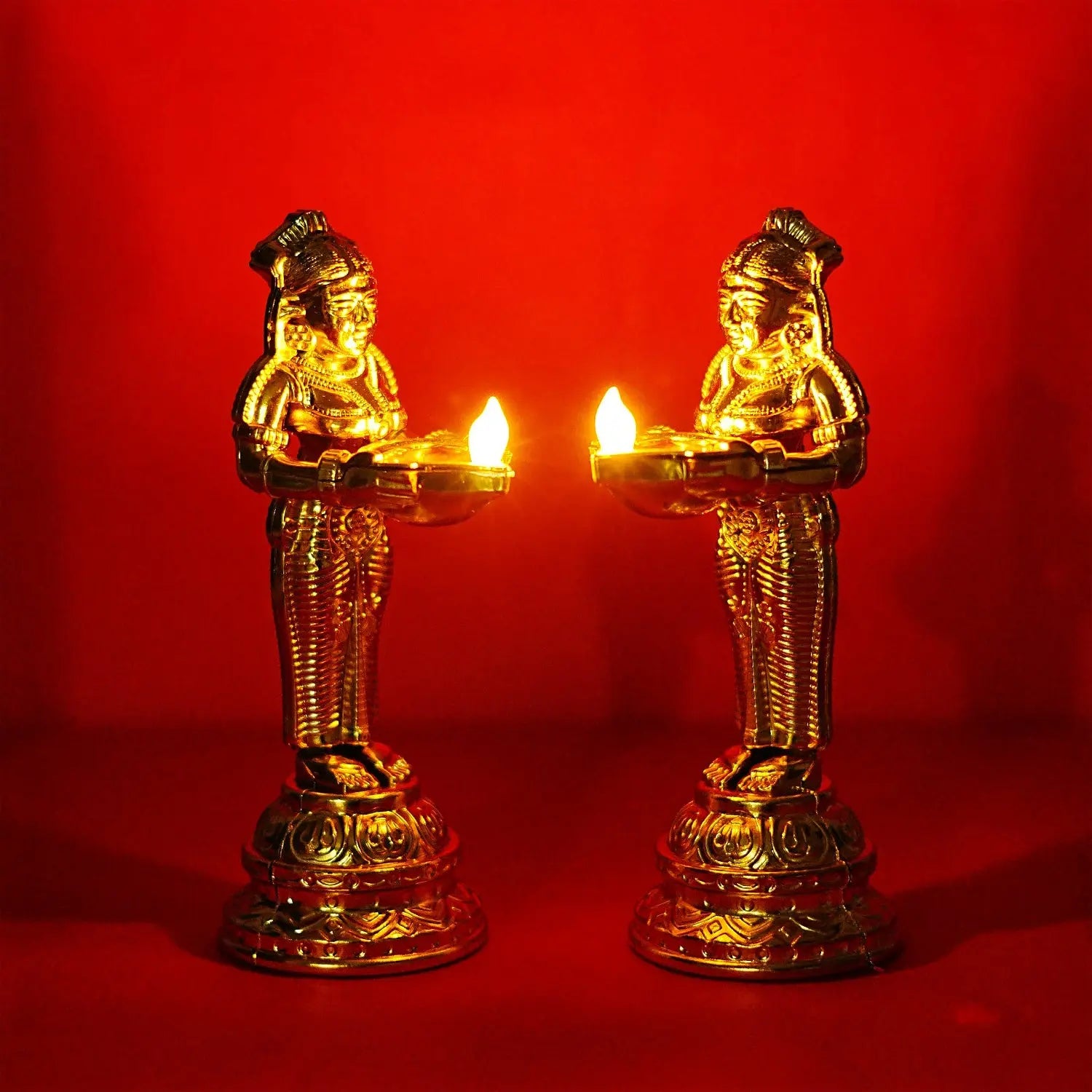 Two gold-colored statues with lit candles on a red background