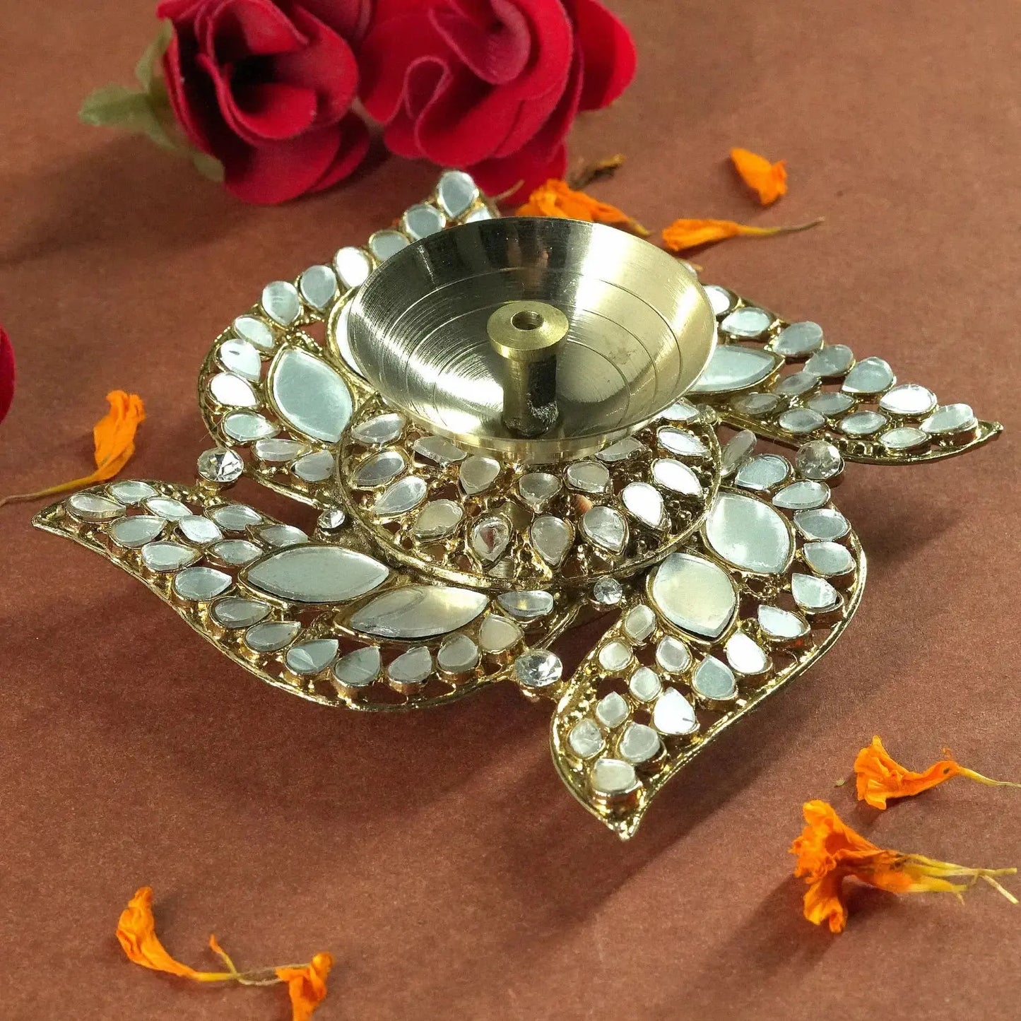 Decorative diya with mirror work on a brown background with flowers.