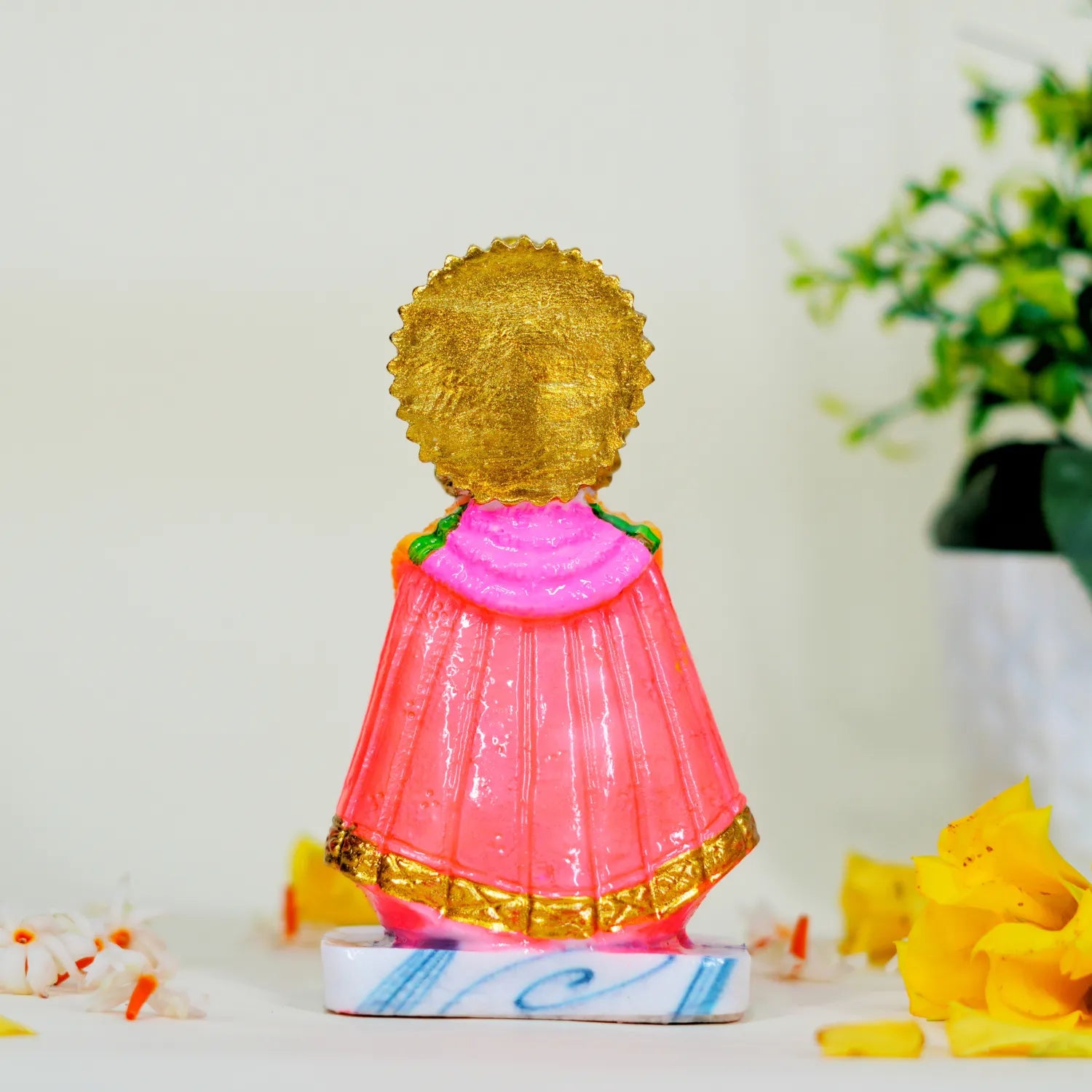 Decorative figurine with gold head and pink body on a white surface with flowers.