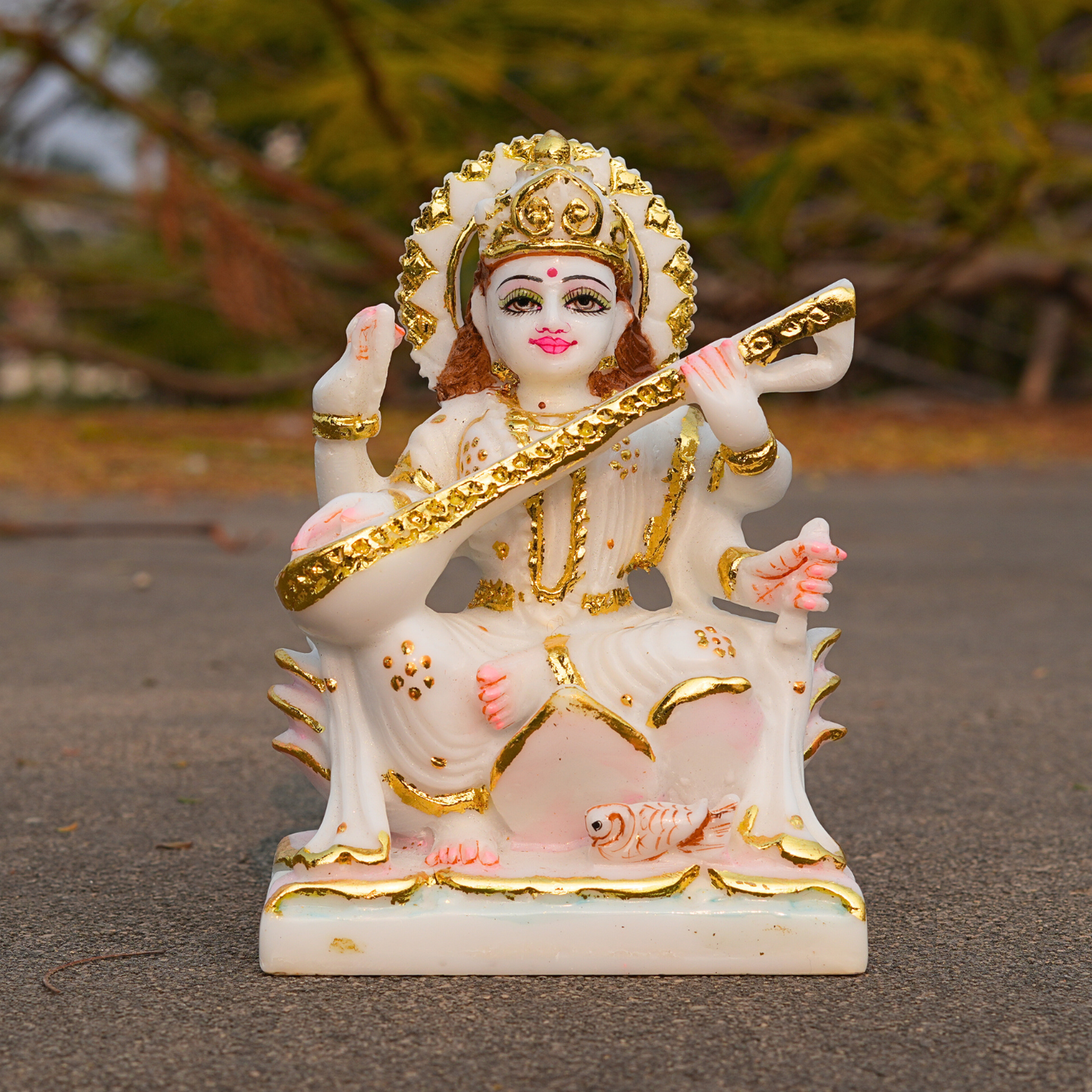 Decorative statue of a deity with gold and pink details on a blurred natural background