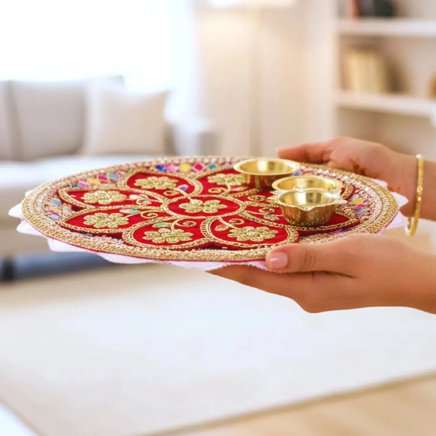 Decorative tray with gold and red design held by a person in a living room.
