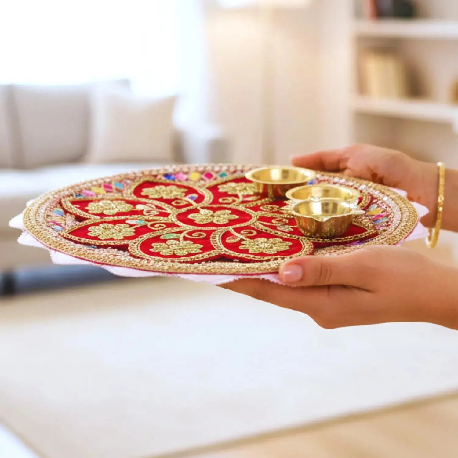 Decorative tray with gold and red design held by a person in a living room.