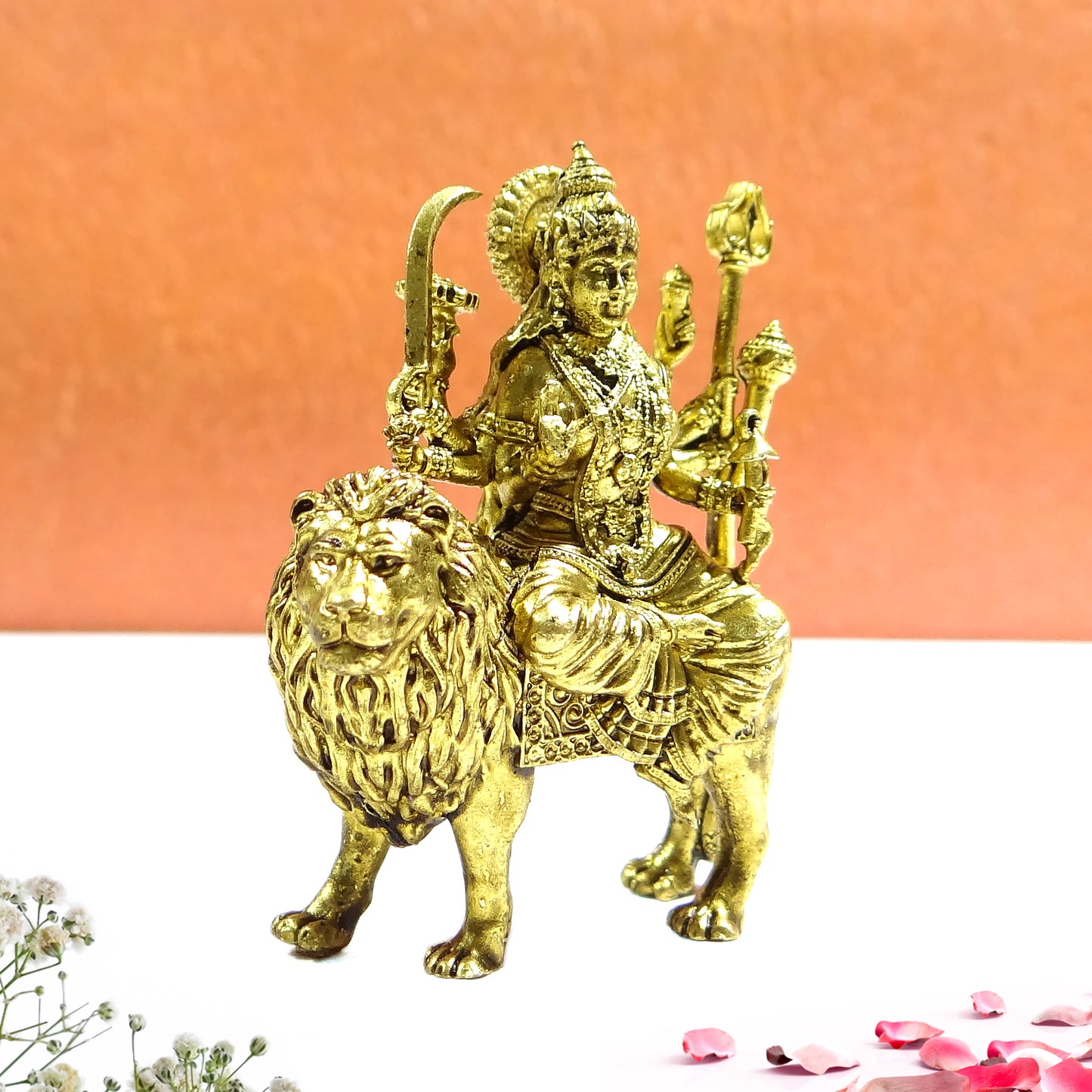 Gold statue of a deity sitting on a lion against an orange background