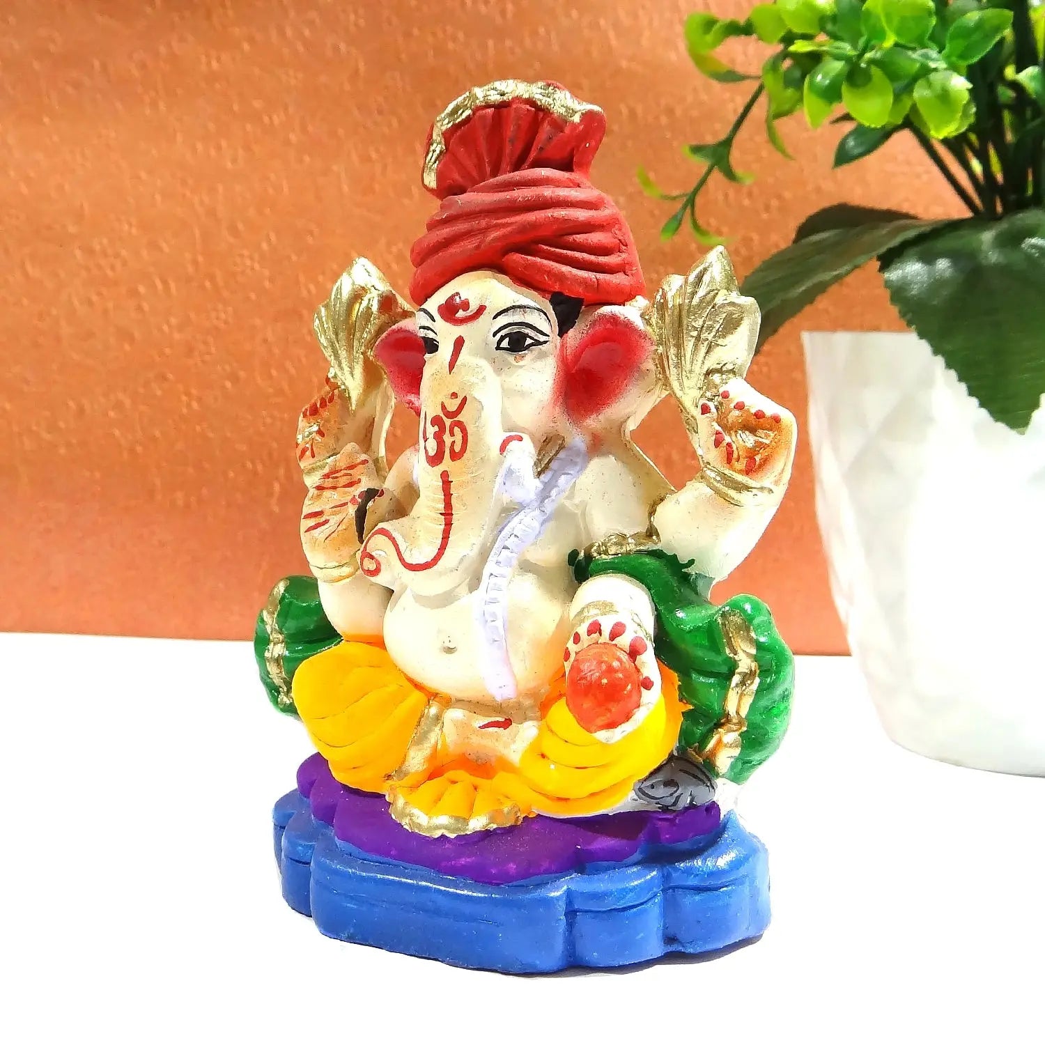 Colorful Ganesha statue with a red turban on a white surface.