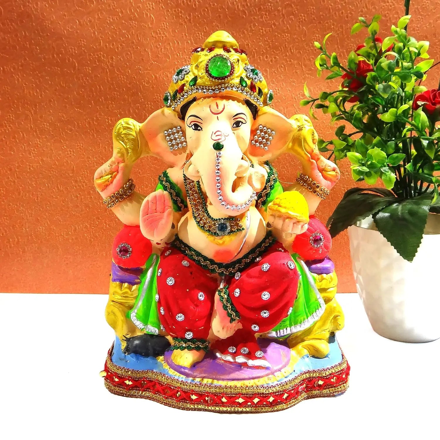 Colorful statue of a deity with jewelry and a plant on an orange background