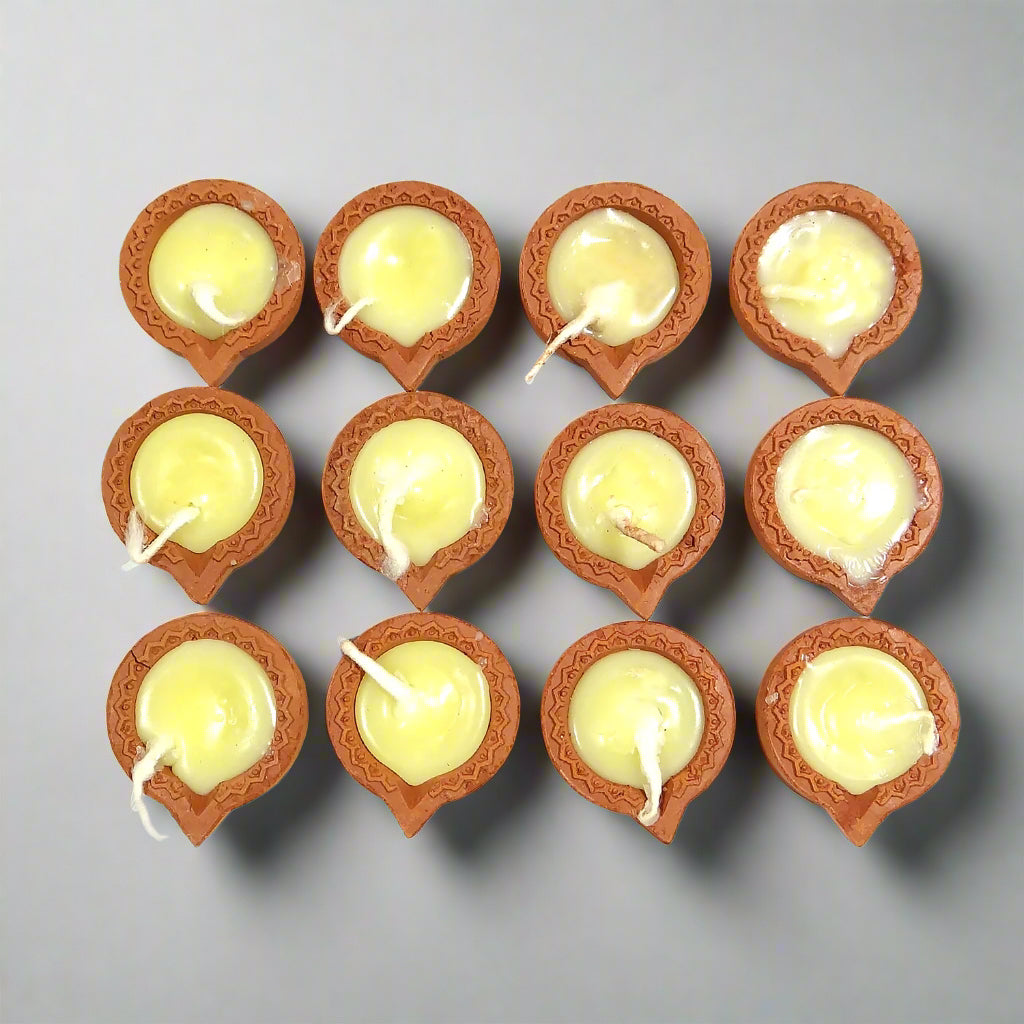 Row of small terracotta lamps with lit candles on a white background
