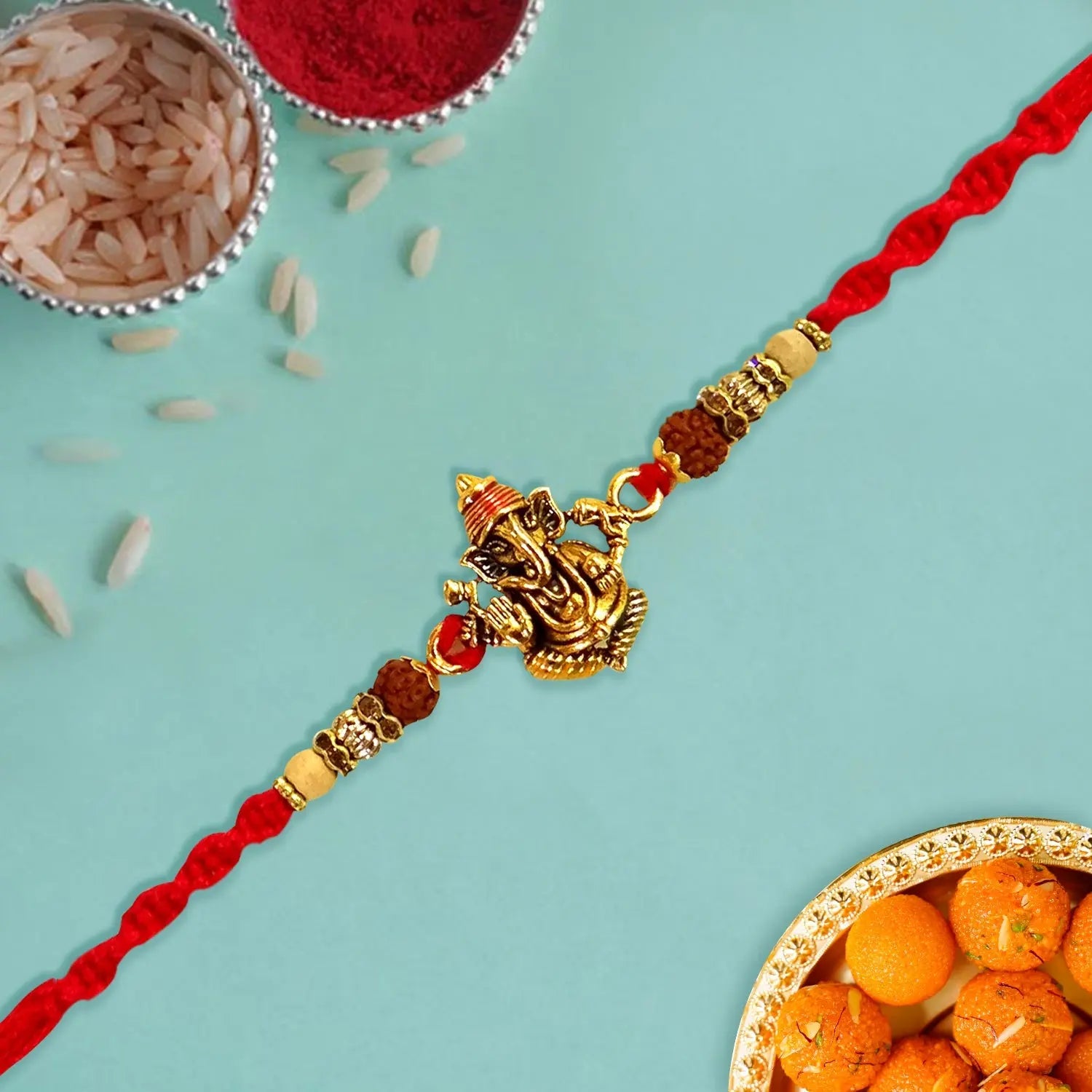 Decorative red and gold Rakhi with Ganesha pendant on a light blue background