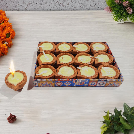 Box of Diwali candles with one lit candle on a decorative surface.