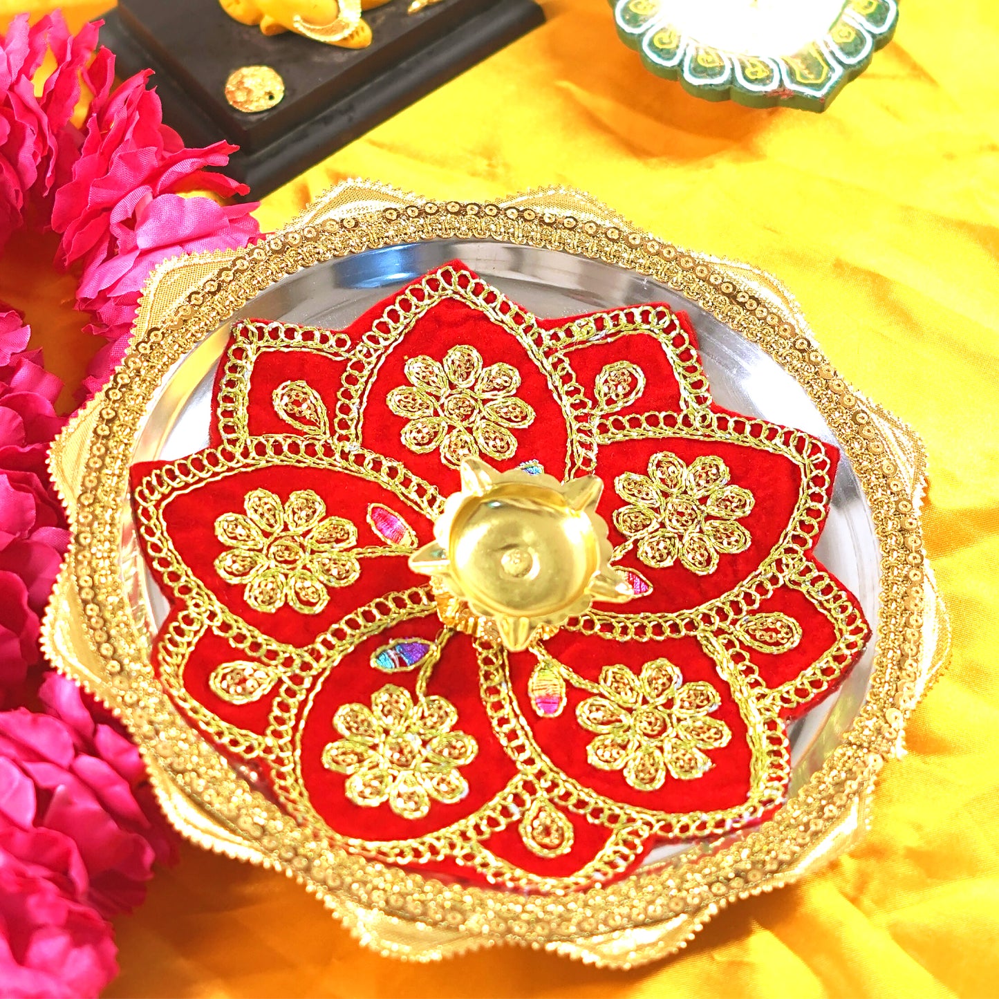 Decorative thali with red and gold design on a yellow fabric background