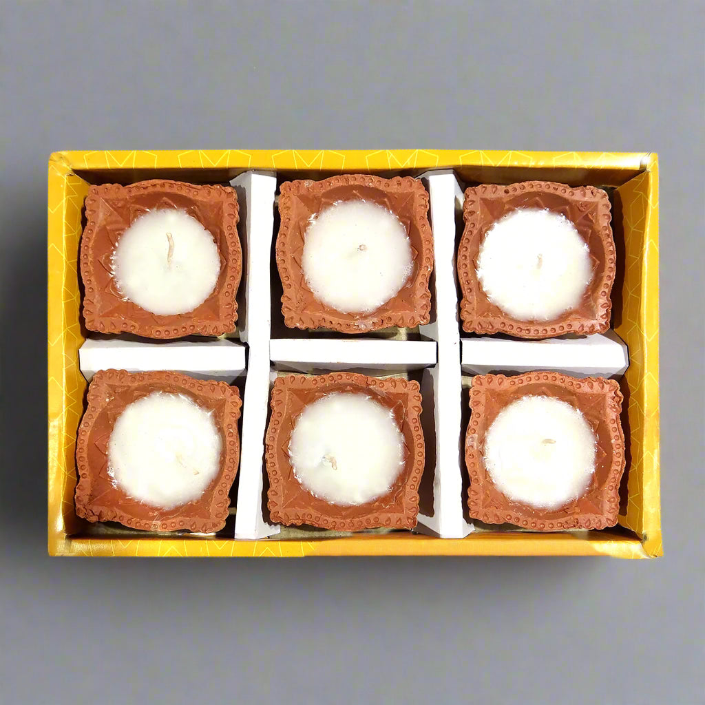 Set of six small candles in decorative holders inside a yellow box on a white background