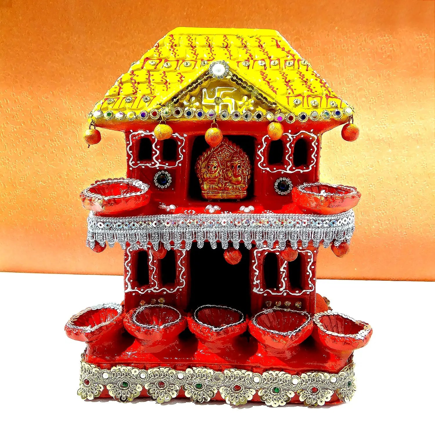 Decorative house-shaped diya with red base and yellow roof on an orange background