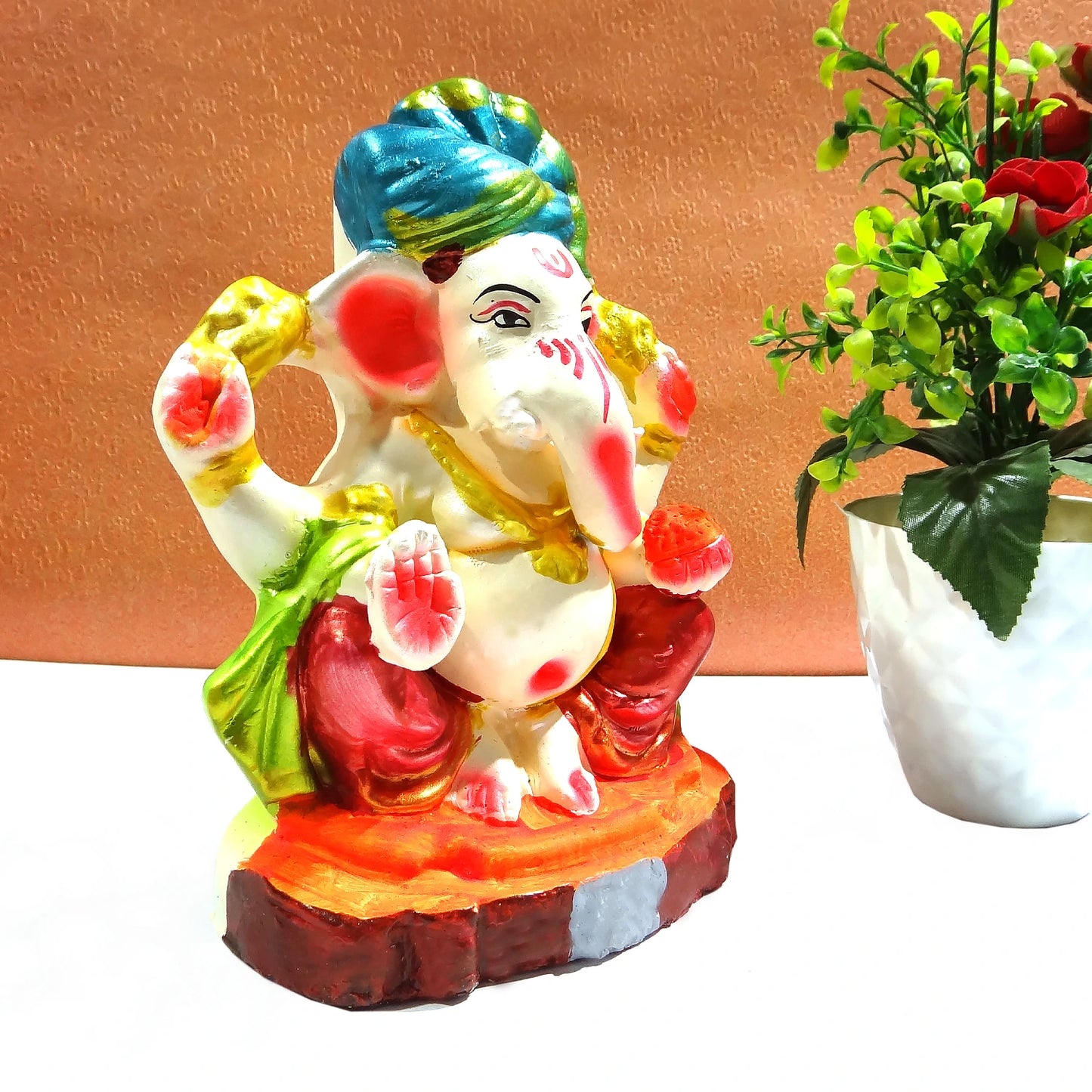 Colorful statue of a deity with a plant on a white surface