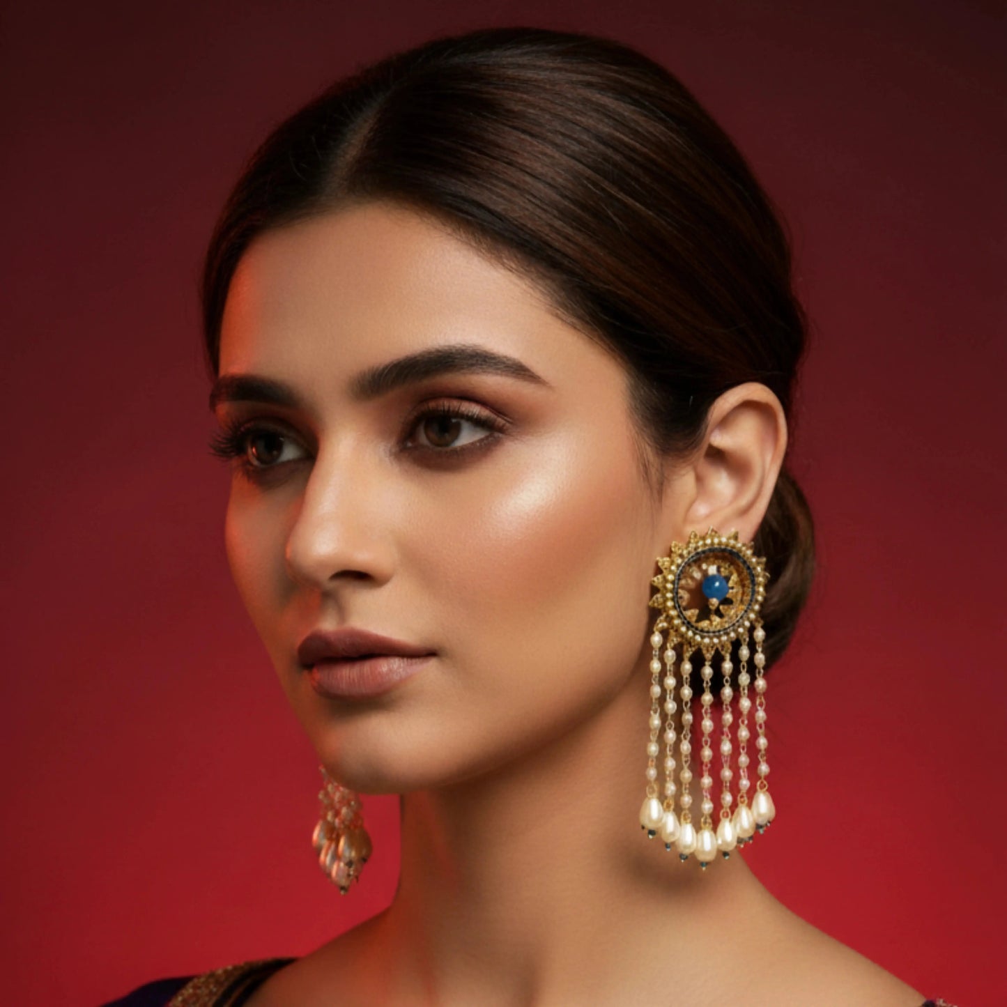 Woman wearing a pair of ornate earrings against a red background