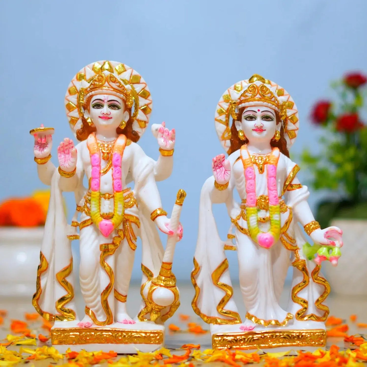 Two ornate statues with gold and pink details on a decorative surface with flowers.