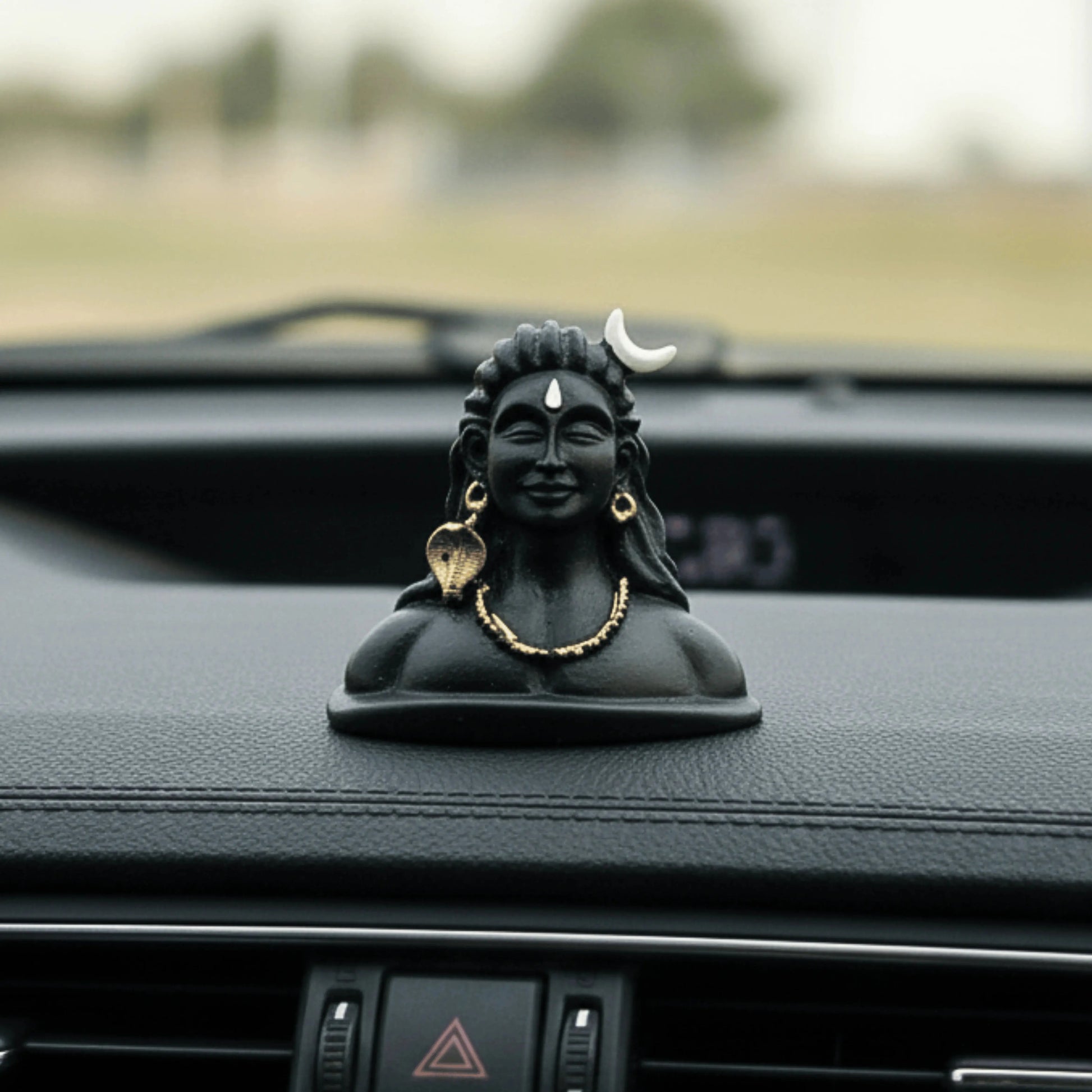 Black figurine of a deity on a car dashboard with a blurred outdoor background