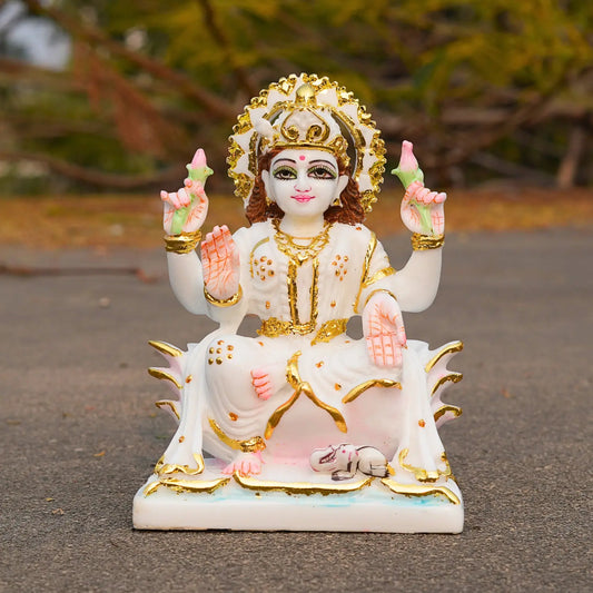 Decorative statue of a seated figure with gold and white attire on a dark surface.