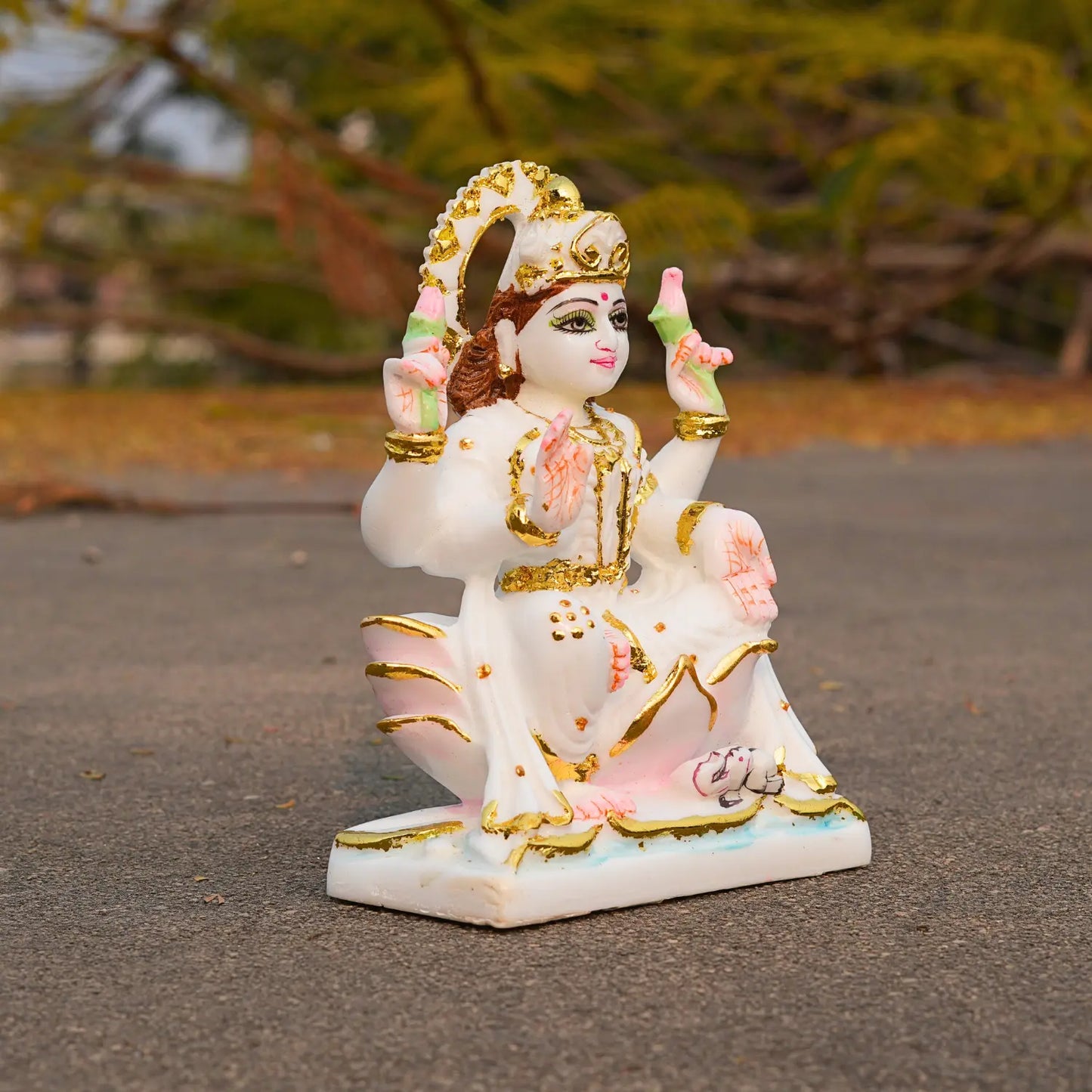 Decorative statue of a seated figure with gold and pink accents on a blurred natural background