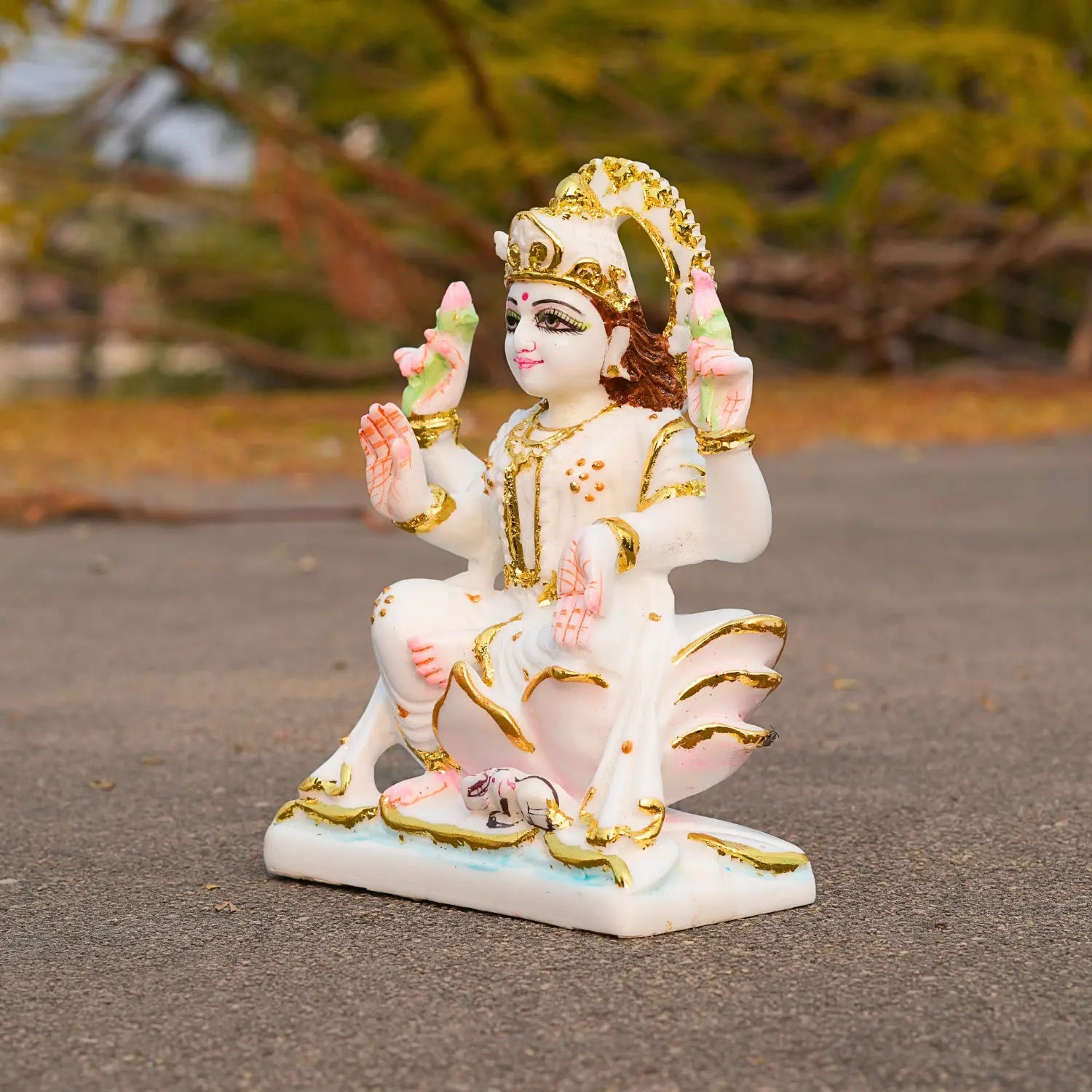 Decorative statue of a seated figure with gold and pink details on a blurred natural background