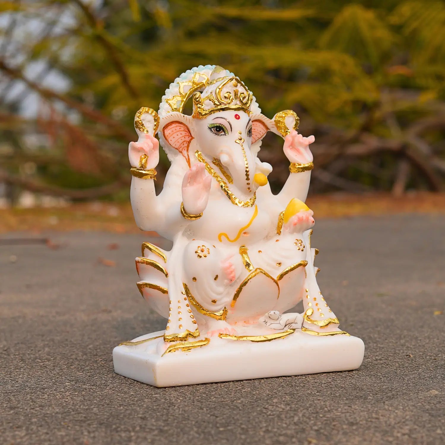 Decorative statue of a deity with gold and white details on a blurred natural background
