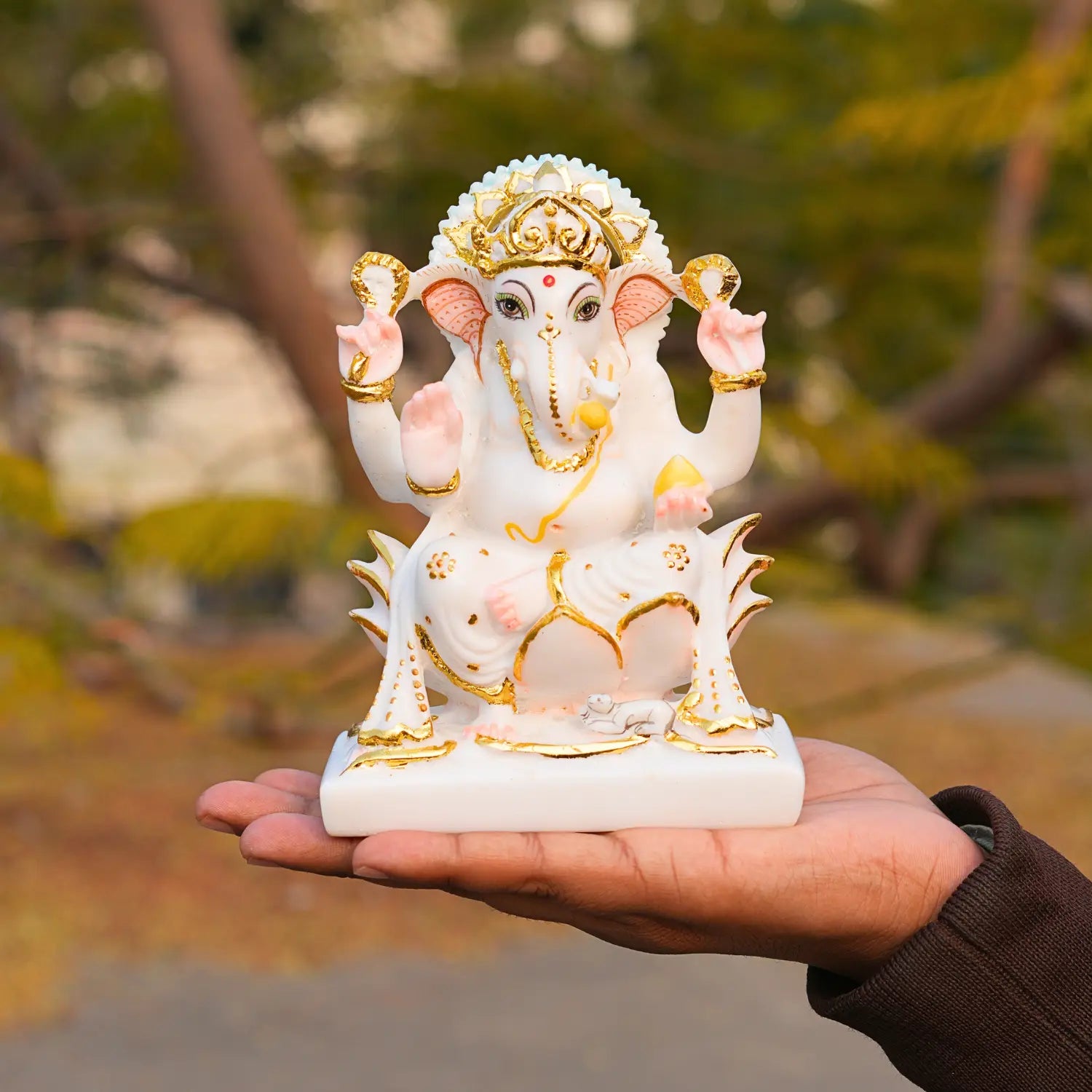 Small statue of a deity held in a hand with a blurred natural background