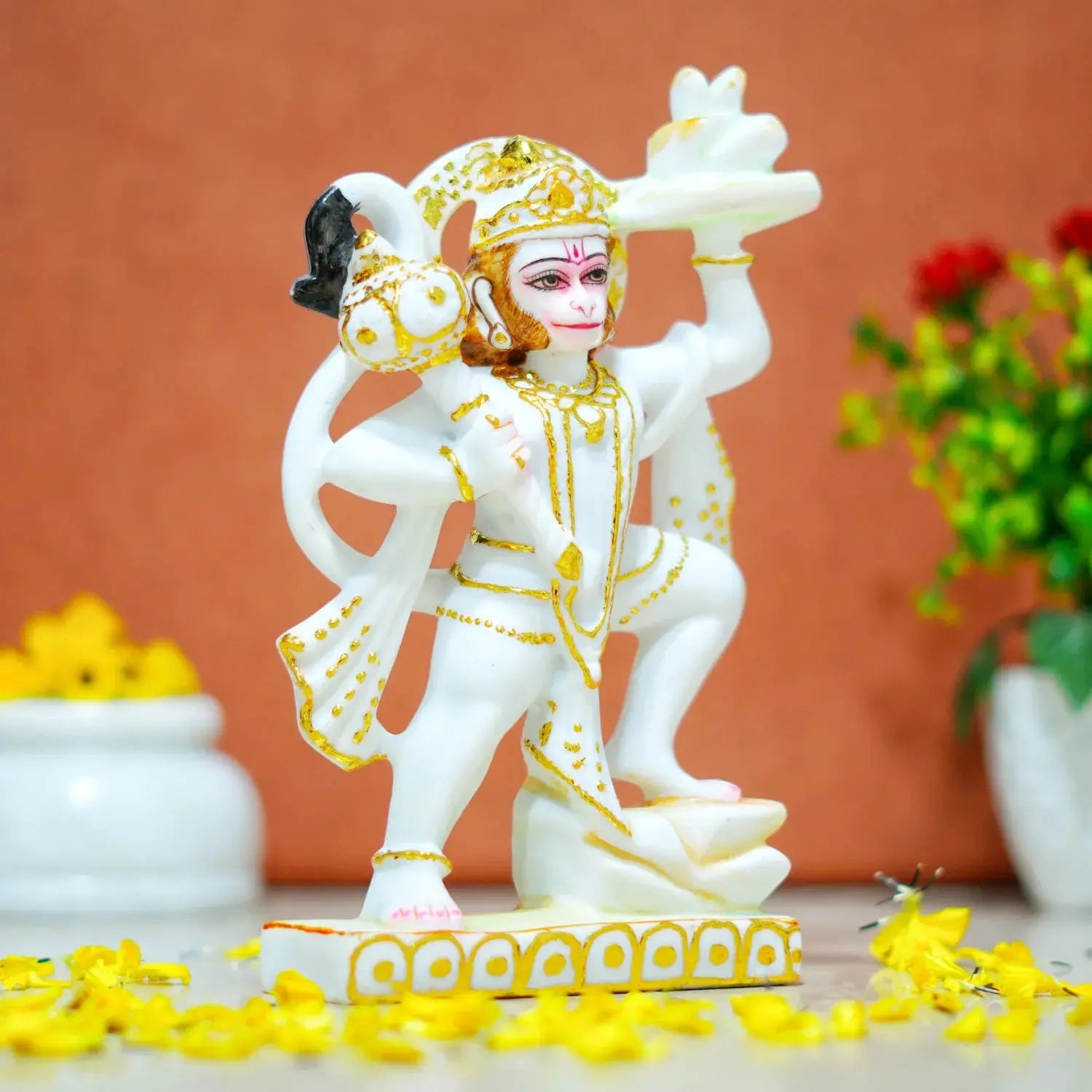 White and gold Hanuman statue on a decorative platform with flowers and a blurred background