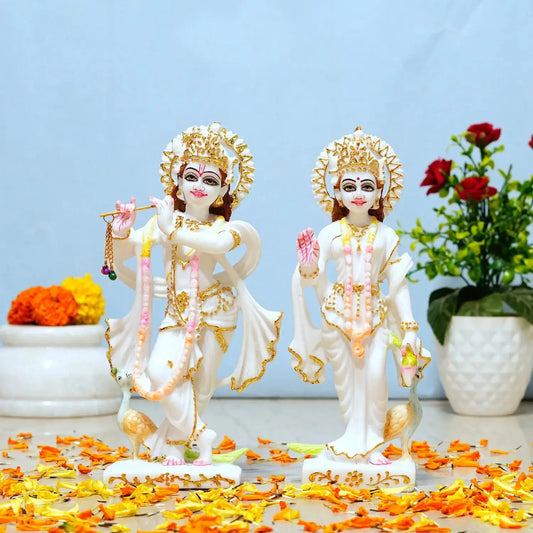 Two deities in white and gold attire with flowers and a plant in the background.