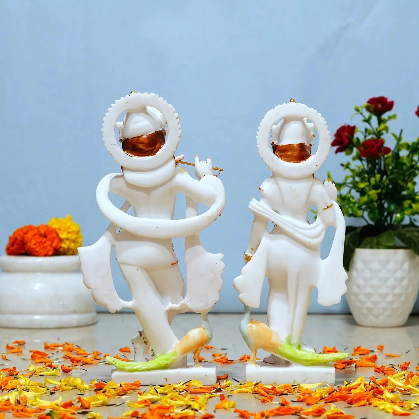 Two white statues of a couple with a blue background and flowers around.